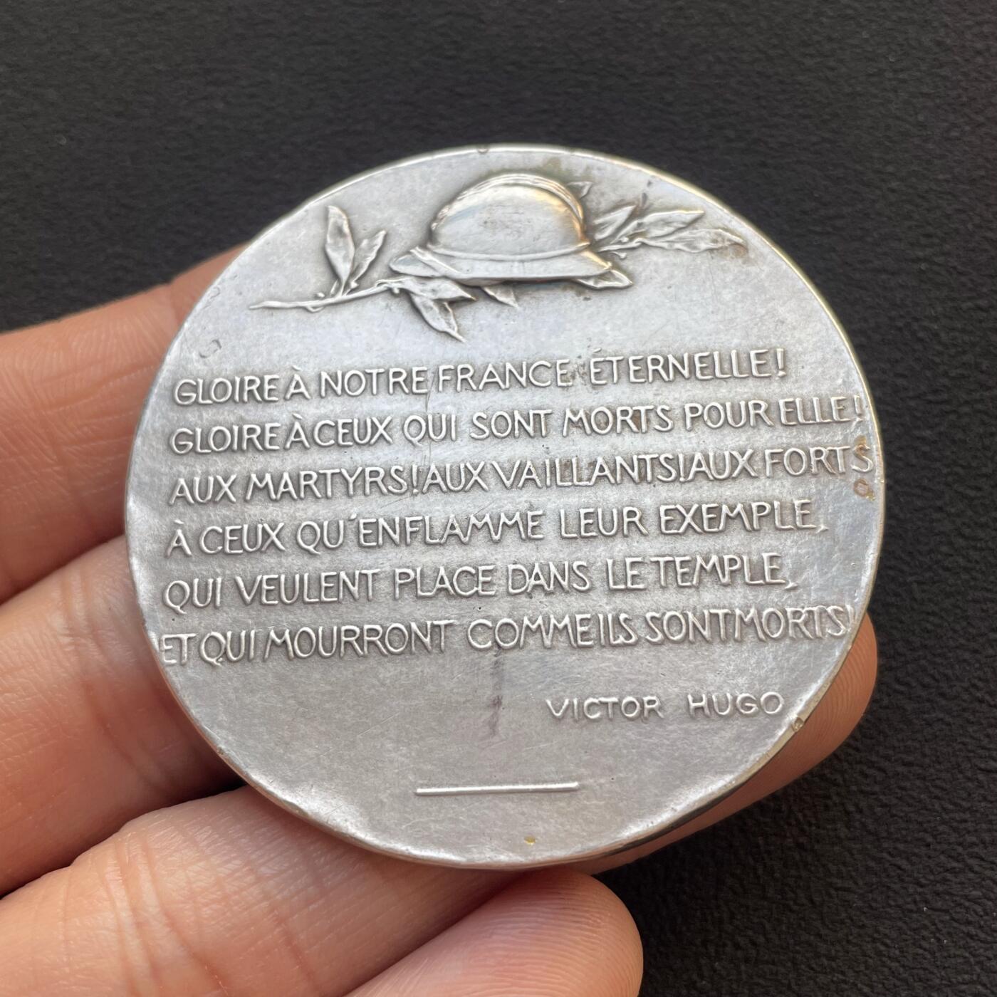 「木头集藏」章牌专场-第65场 1914年法国一战爱国主义纪念银章，直径：50mm，56.2 g，边铭：菱形厂标 野猪头银标 ARGENT，背面刻有维克多·雨果《为法国而死》（Morts pour la France）中的诗句：“荣耀归于我们永恒的法兰西！荣耀归于为她牺牲的人们！致殉道者、勇者、强者，致那些被他们的榜样所激励，渴望在圣殿中拥有一席之地，并将如他们般赴死的人”。带有木质展示架，可正常使用。