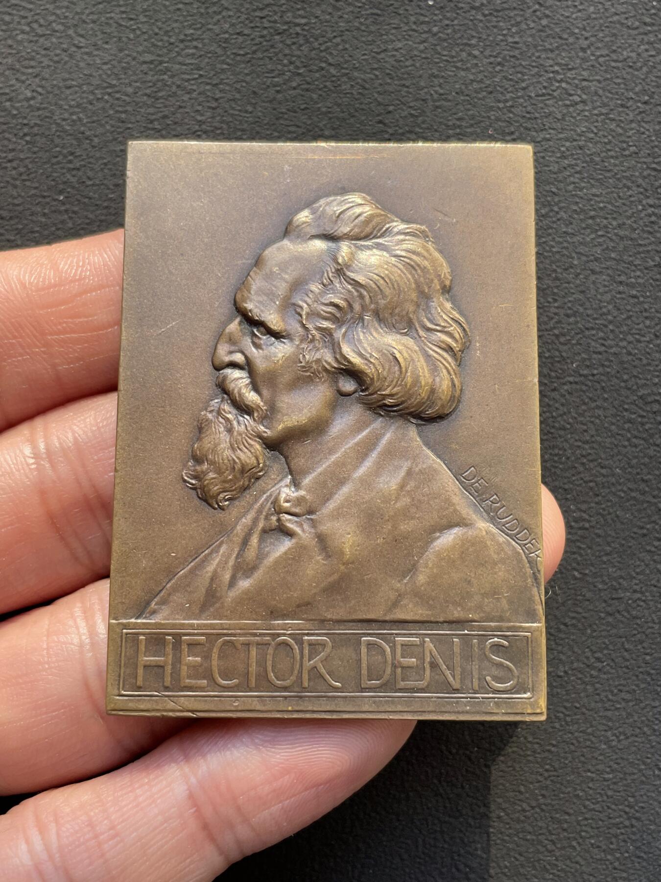 「木头集藏」章牌专场-第65场 比利时布鲁塞尔自由大学教授赫克托·丹尼斯纪念章， 尺寸：59×42mm，81.5g。 赫克托·丹尼斯教授于1878年至1912年间，在自由大学担任教职34年。这枚长方形铜章就是为纪念他的卓越奉献而定制的。 正面是教授的左侧胸像，下方铭文是他的姓名。背面为知识女神点向象征光明的太阳图案，上方三行铭文意为“自由大学”“教授”“1878年至1912年”。