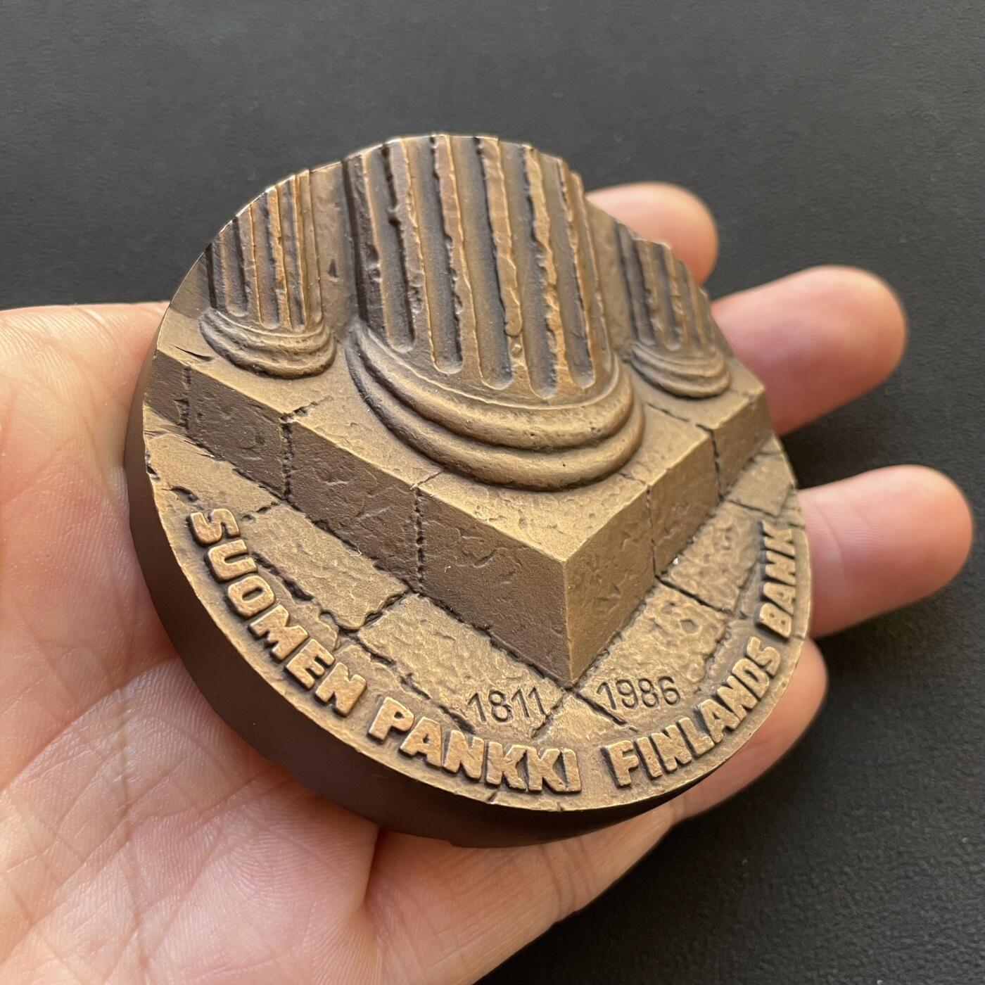 「木头集藏」章牌专场-第65场 芬兰银行（芬兰中央银行）175周年纪念加厚纪念大铜章，直径：70 mm，403g，特别加厚，超高浮雕，厚重压手。正面图案为高浮雕罗马柱基座，象征央行是芬兰国家的重要支柱基础。背面是抽象的芬兰地图高浮雕造型。 芬兰银行是芬兰共和国的中央银行，也是欧洲中央银行系统的成员。