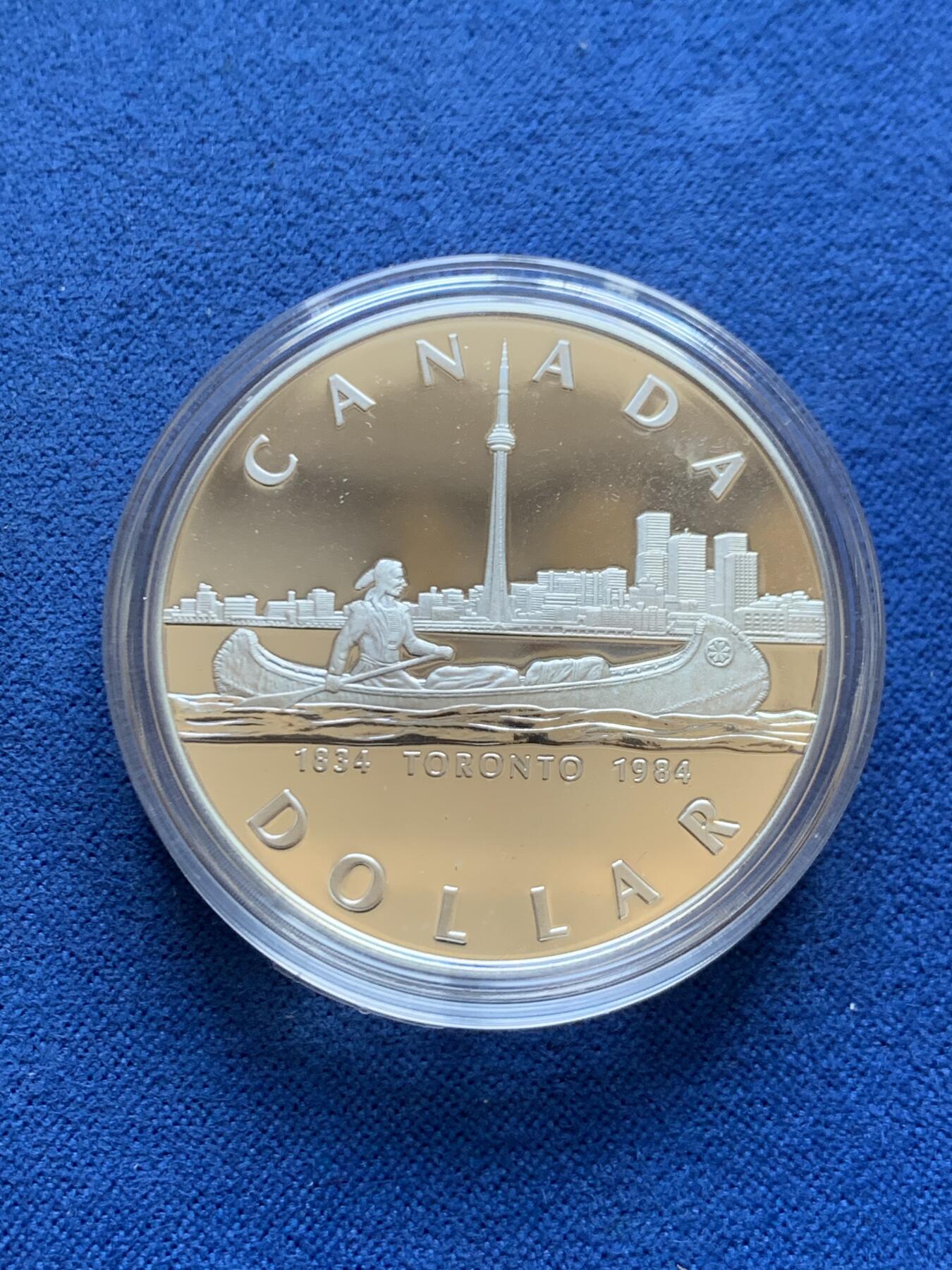 《竞宝斋》第453场 周日，周一 2场连拍 （全场包邮，欢迎送拍） 加拿大1984年多伦多市成立100周年纪念银币，直径36mm ，重23.3g 。正面为伊丽莎白二世女王年轻时右向胸像，背面为水面划船的印第安人背景为多伦多轮廓。原盒，类精制银币，状态极佳。