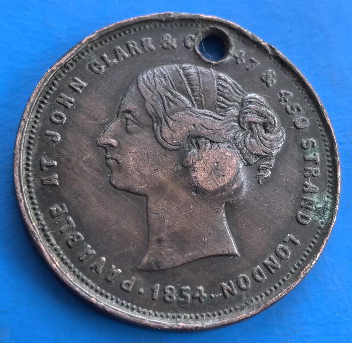 外国优质老铜币高银银币，周六九点倒数截拍，满百包邮，持续收拍 英国1854 年约翰・克拉克公司代用铜币，直径34.5mm，18克，正面维多利亚女王像，环刻公司名与伦敦地址，见证 19 世纪商业生态。背面图案虽磨损，打孔痕迹添历史层次。属维多利亚时期商业代币，承载当时广告与货币代用文化，小众收藏佳品，为研究近代英国商业史提供独特视角 。