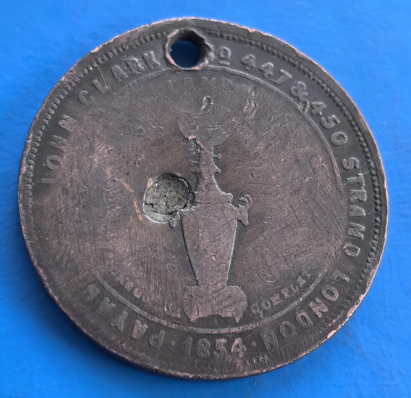 外国优质老铜币高银银币，周六九点倒数截拍，满百包邮，持续收拍 英国1854 年约翰・克拉克公司代用铜币，直径34.5mm，18克，正面维多利亚女王像，环刻公司名与伦敦地址，见证 19 世纪商业生态。背面图案虽磨损，打孔痕迹添历史层次。属维多利亚时期商业代币，承载当时广告与货币代用文化，小众收藏佳品，为研究近代英国商业史提供独特视角 。