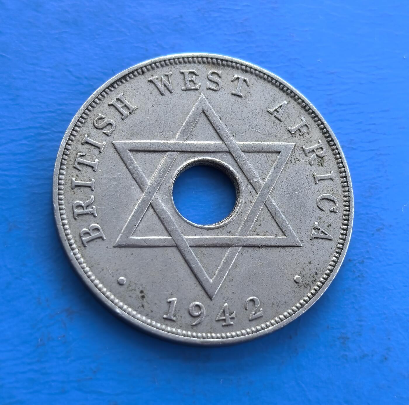 外国优质老铜币高银银币，周六九点倒数截拍，满百包邮，持续收拍 英属西非1942 年 1 便士，中孔设计别致。正面镌乔治六世王冠、王室铭文与阿拉伯文，背面六芒星环绕，融合殖民与多元文化符号。诞生于二战关键期，见证英属西非历史，铜镍包浆凝岁月痕，属殖民币稀缺标本，解码战时脉络，收藏兼具故事性与设计价值 。