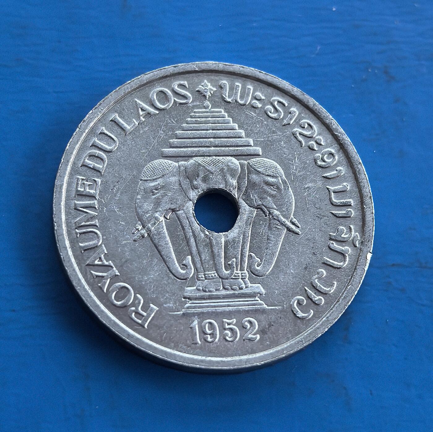 外国优质老铜币高银银币，周六九点倒数截拍，满百包邮，持续收拍 老挝王国1952年20 分，独特穿孔设计。正面双象拱卫佛塔，融合宗教与王室符号；背面花叶纹呼应民俗。包浆自然，见证老挝君主制阶段。属东南亚小众币，承载中南半岛文化印记，稀缺异域属性，是收藏拓展视野、解码老挝历史的独特标的 。