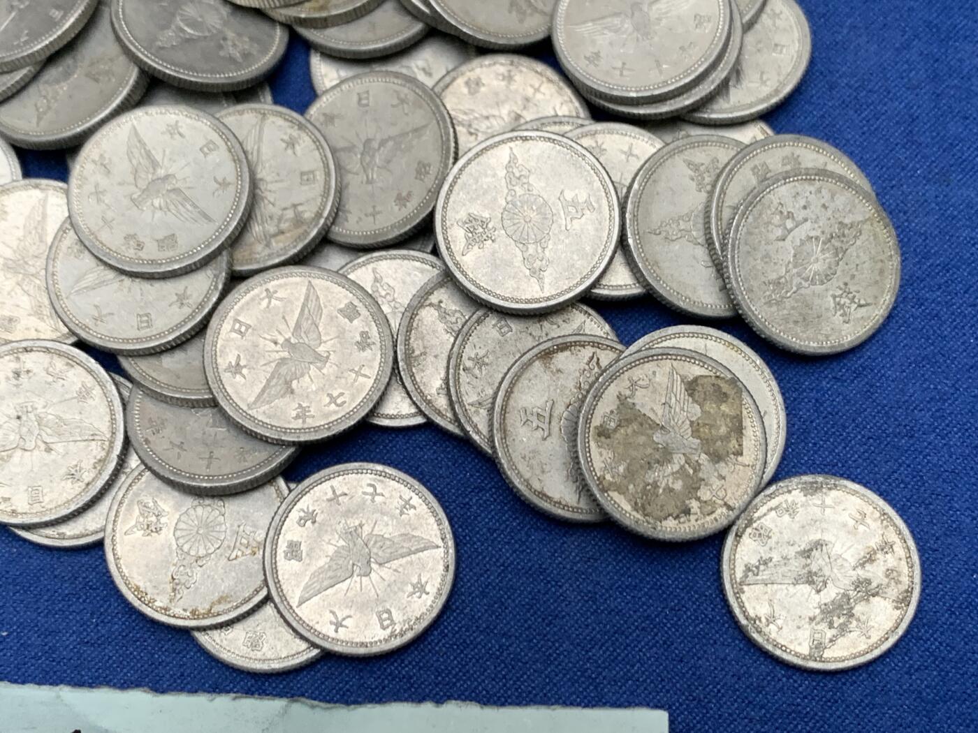 《竞宝斋》第454场 周日，周一 2场连拍 （全场包邮，欢迎送拍） 约54枚一组 日本战时1940-1943年飞鸟（金鵄）五钱铝制硬币，彼时日本深陷战争泥潭，原本的铜质五钱被迫停产改为铝币，该币正面是日本皇室的十六瓣八重表菊纹，外环镌刻国号与昭和年号；背面主体为象征日本的金鵄（飞鸟）图案，搭配“五钱”面值，1943年因铝资源彻底枯竭停铸。