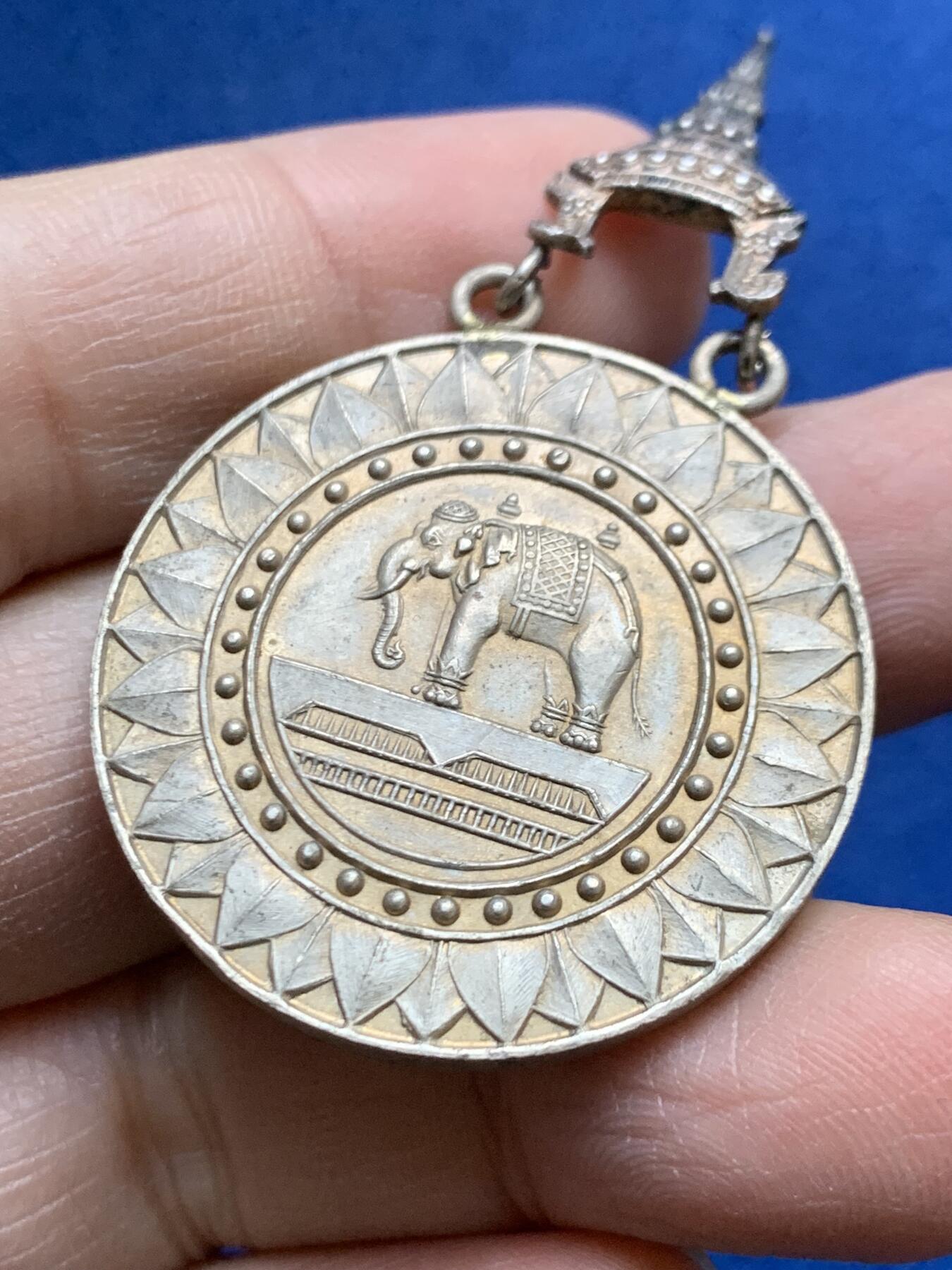 《竞宝斋》第454场 周日，周一 2场连拍 （全场包邮，欢迎送拍） 原盒 泰国银质白象宝塔勋章，历史可以追溯到1861年由当时的君主拉玛四世创立。约上世纪中期发行，佛塔背面有泰文戳记，裸章重约：21.5克。原盒原绶带。这个勋章专门为表彰那些在艺术、科学、商业、外交等领域有杰出贡献的知名人士，状态如图，近未使用品，疑似背面挂环脱落，介意勿拍！