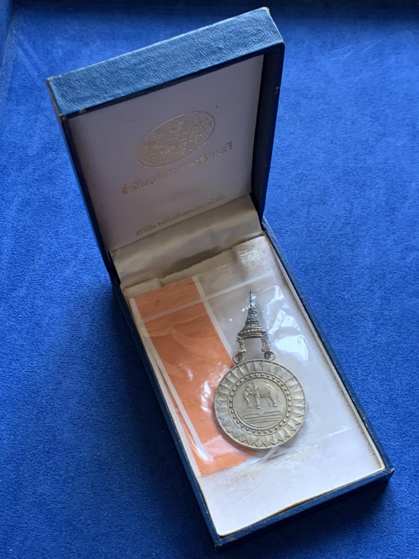 《竞宝斋》第454场 周日，周一 2场连拍 （全场包邮，欢迎送拍） 原盒 泰国银质白象宝塔勋章，历史可以追溯到1861年由当时的君主拉玛四世创立。约上世纪中期发行，佛塔背面有泰文戳记，裸章重约：21.5克。原盒原绶带。这个勋章专门为表彰那些在艺术、科学、商业、外交等领域有杰出贡献的知名人士，状态如图，近未使用品，疑似背面挂环脱落，介意勿拍！