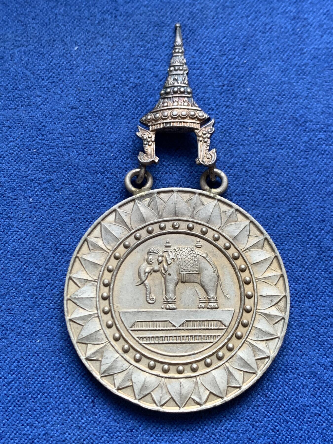 《竞宝斋》第454场 周日，周一 2场连拍 （全场包邮，欢迎送拍） 原盒 泰国银质白象宝塔勋章，历史可以追溯到1861年由当时的君主拉玛四世创立。约上世纪中期发行，佛塔背面有泰文戳记，裸章重约：21.5克。原盒原绶带。这个勋章专门为表彰那些在艺术、科学、商业、外交等领域有杰出贡献的知名人士，状态如图，近未使用品，疑似背面挂环脱落，介意勿拍！