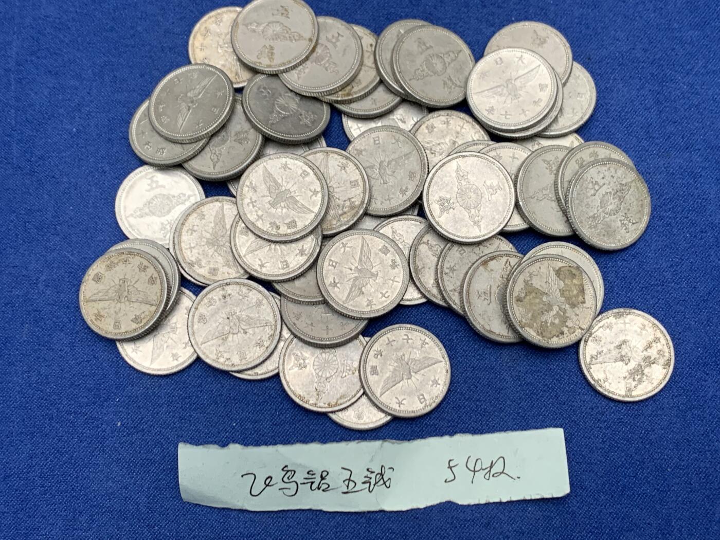 《竞宝斋》第454场 周日，周一 2场连拍 （全场包邮，欢迎送拍） 约54枚一组 日本战时1940-1943年飞鸟（金鵄）五钱铝制硬币，彼时日本深陷战争泥潭，原本的铜质五钱被迫停产改为铝币，该币正面是日本皇室的十六瓣八重表菊纹，外环镌刻国号与昭和年号；背面主体为象征日本的金鵄（飞鸟）图案，搭配“五钱”面值，1943年因铝资源彻底枯竭停铸。