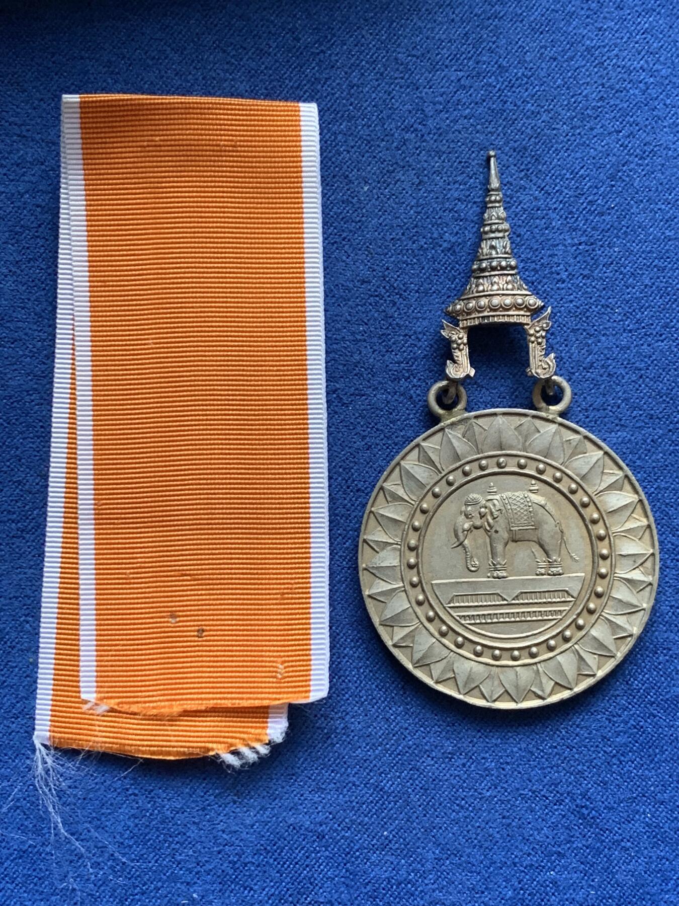 《竞宝斋》第454场 周日，周一 2场连拍 （全场包邮，欢迎送拍） 原盒 泰国银质白象宝塔勋章，历史可以追溯到1861年由当时的君主拉玛四世创立。约上世纪中期发行，佛塔背面有泰文戳记，裸章重约：21.5克。原盒原绶带。这个勋章专门为表彰那些在艺术、科学、商业、外交等领域有杰出贡献的知名人士，状态如图，近未使用品，疑似背面挂环脱落，介意勿拍！