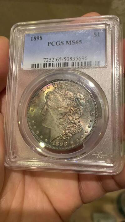《竞宝斋》第455场 周日，周一 2场连拍 （全场包邮，欢迎送拍） PCGS MS65 美国1898年摩根一美元银币，1898年年份较少，本枚为标准卷首彩，美轮美奂，绚丽五彩，值得重新送评