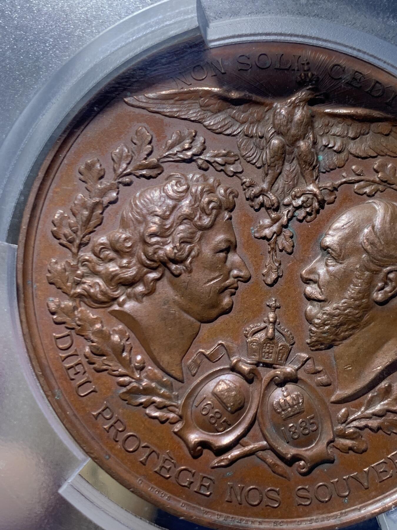 《竞宝斋》第455场 周日，周一 2场连拍 （全场包邮，欢迎送拍） PCGS SP62 德国普鲁士1885年纪念柏林法国教区成立200周年大铜章，少见品。正面图案：花枝环绕下，弗里德里希大帝和威廉一世的侧像，在两顶加冕皇冠的衬托下，冠冕头鹰两翼张开，气势非凡。反面图案：波卢西亚女神手握剑和盾牌，守护着孩子们。精美的高浮雕铜章，极具收藏价值。加大加厚盒