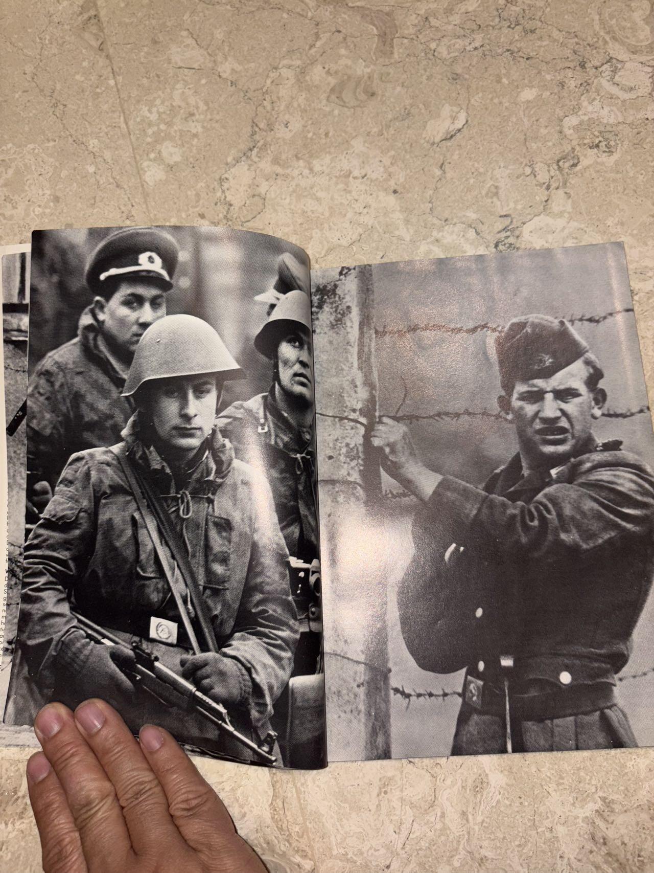 盛世勋华——号角文化勋章邮票专场拍卖第298期 德国柏林墙文献《发生在墙边的事》，附带荷兰语报纸对柏林墙相关历史的专题报道，记录了1961年8月13日柏林墙修建至1989年倒塌期间，西柏林周边封锁带的发展与关键事件。全书127页，采用黑白纪实摄影，左侧是守卫柏林墙的士兵形象，右侧是柏林墙相关事件的纪实小图（如越墙尝试、热气球逃亡、地标建筑等），直观展现冷战时期柏林的分裂状态。