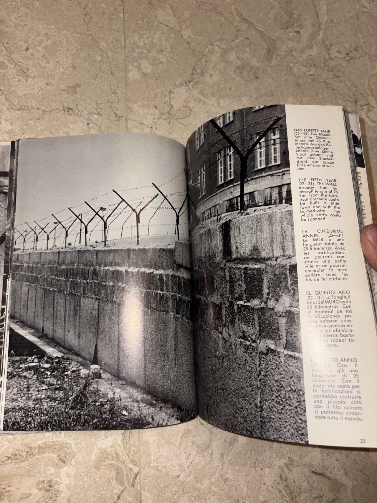 盛世勋华——号角文化勋章邮票专场拍卖第298期 德国柏林墙文献《发生在墙边的事》，附带荷兰语报纸对柏林墙相关历史的专题报道，记录了1961年8月13日柏林墙修建至1989年倒塌期间，西柏林周边封锁带的发展与关键事件。全书127页，采用黑白纪实摄影，左侧是守卫柏林墙的士兵形象，右侧是柏林墙相关事件的纪实小图（如越墙尝试、热气球逃亡、地标建筑等），直观展现冷战时期柏林的分裂状态。