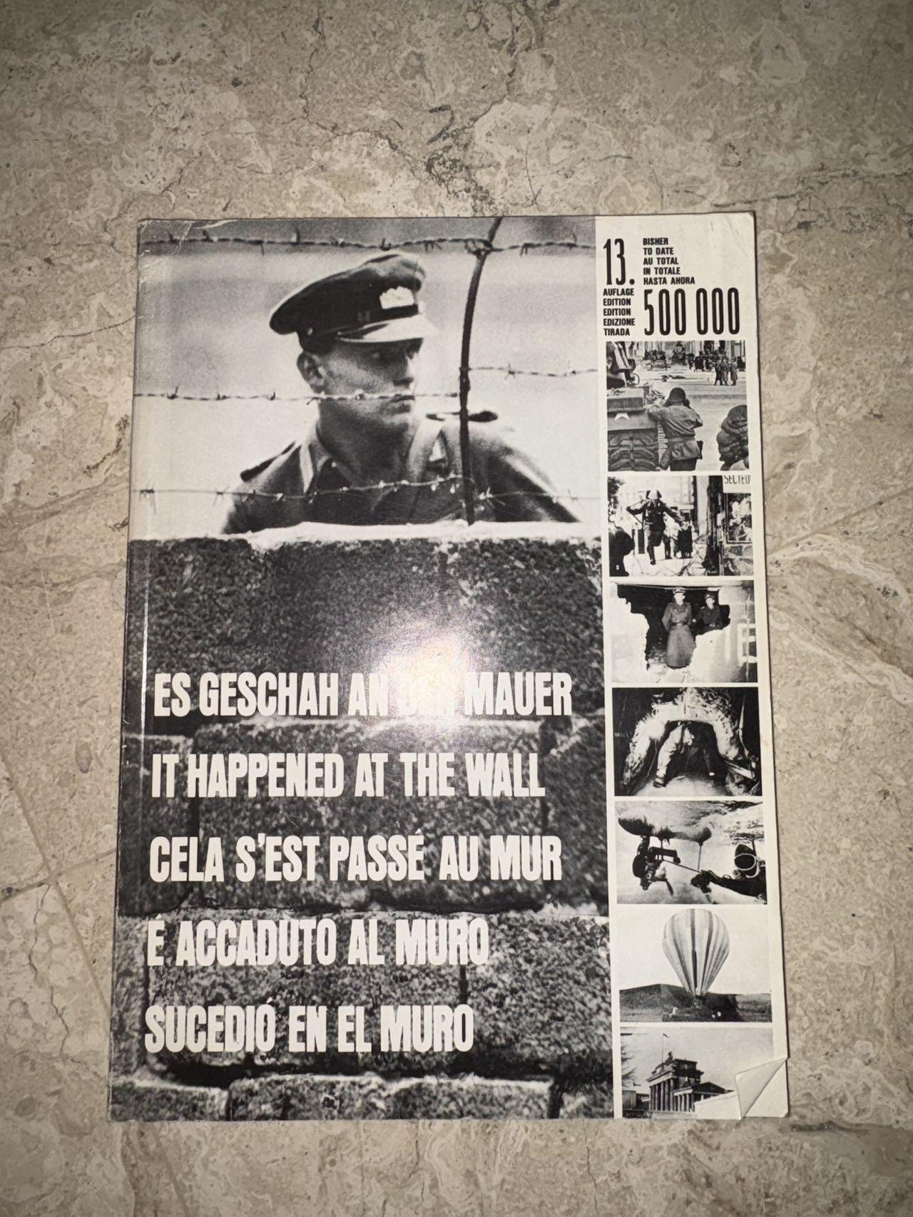 盛世勋华——号角文化勋章邮票专场拍卖第298期 德国柏林墙文献《发生在墙边的事》，附带荷兰语报纸对柏林墙相关历史的专题报道，记录了1961年8月13日柏林墙修建至1989年倒塌期间，西柏林周边封锁带的发展与关键事件。全书127页，采用黑白纪实摄影，左侧是守卫柏林墙的士兵形象，右侧是柏林墙相关事件的纪实小图（如越墙尝试、热气球逃亡、地标建筑等），直观展现冷战时期柏林的分裂状态。