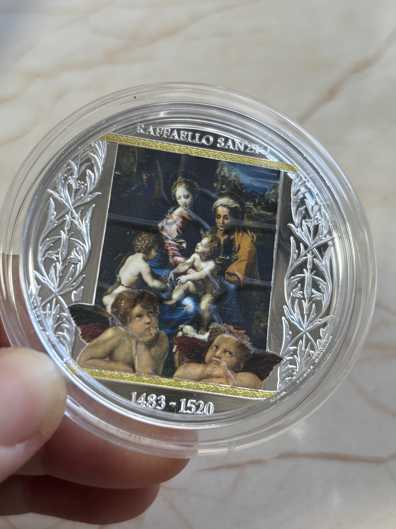 第187期拍卖 喀麦隆2020年，拉斐尔 名画-《圣母玛利亚一家》(神圣之家或母与子)，加大(直径达50mm)、镀金, 彩色精制银币. 盒证全. 发行仅300枚. 颜色有凸色现象(由于特有的着色工艺),属于正常现象. 超级精美漂亮银币.