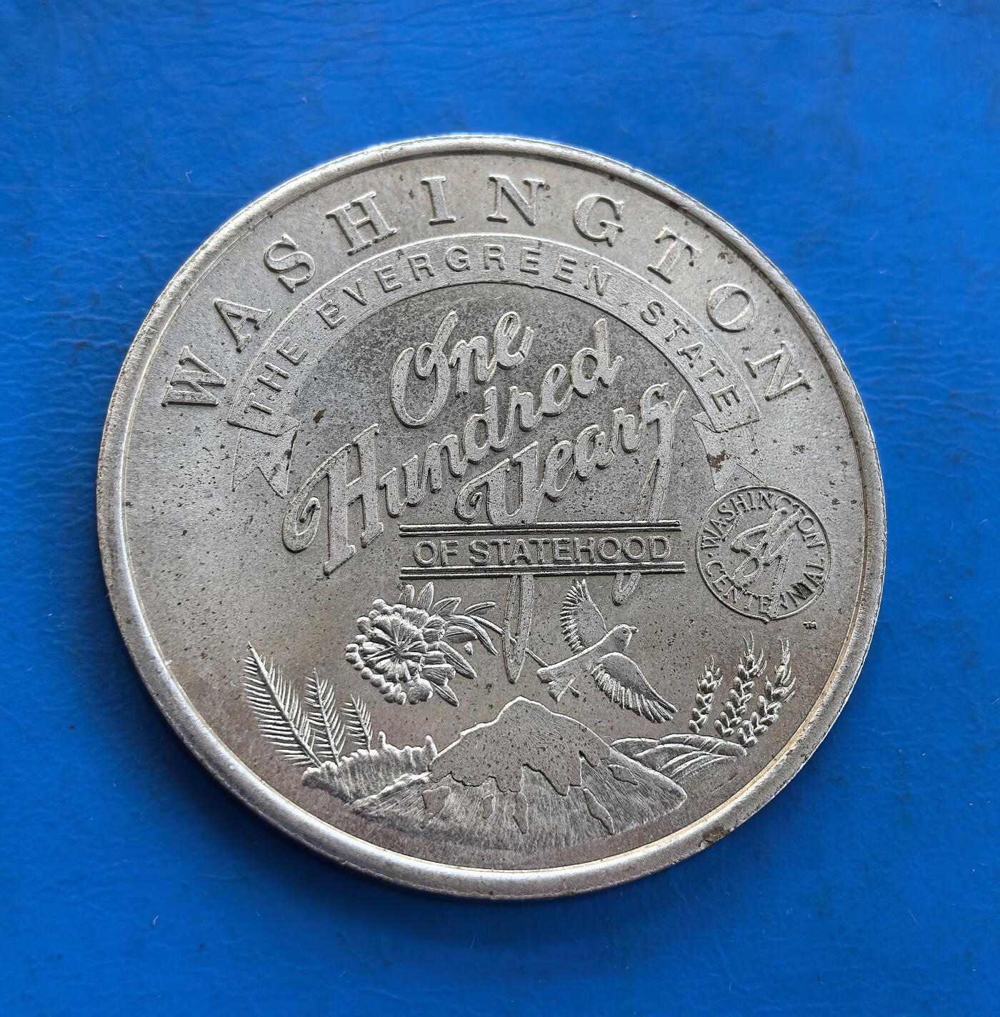 外国优质银币南亚香港苏联等专场，周六九点倒数截拍，满百包邮，持续收拍 发行量仅2000枚，美国华盛顿州考利茨县发行的建州百年纪念币（直径40mm，重21.8克）搭配州花、雷尼尔山与飞鸟浮雕；呈现当地标志性的松树、山脉景观。细腻包浆承载地域文化，兼具纪念与收藏价值，是美国地方纪念币的特色品类。