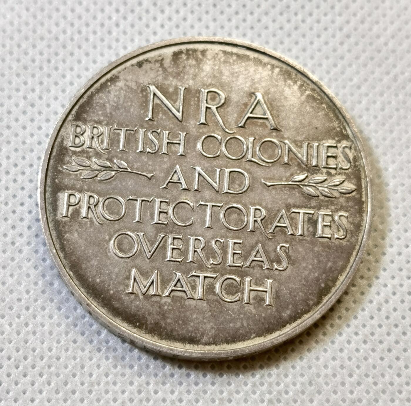 甄臻铺-世界币章拍卖（第48期）精品场拍品征集中，送拍享返佣金等优惠多多 1938年英国NRA(国家步枪协会)海外比赛纪念银章，正面是狮子和鹰的浮雕图案，中间是盾形徽章，背面刻有NRA BRITISH COLONIES AND PROTECTORATES OVERSEAS MATCH字样。直径41.3毫米，重43.3克，边缘刻有获奖者及日期字样