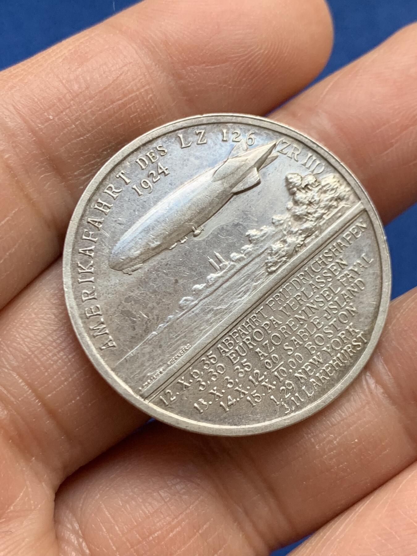 《竞宝斋》第459场 周日，周一，2场连拍 （全场包邮）欢迎送拍 德国雨果·埃克纳纪念银章，他是20世纪初飞艇技术的重要推动者，曾担任齐柏林飞艇公司的负责人，并亲自驾驶“兴登堡号”等著名飞艇完成多次跨大西洋飞行。该章背面详细列出了飞艇的行程时间表，包括从弗里德里希港出发、离开欧洲、经过亚速尔群岛法亚尔、到达萨布尔岛、波士顿、纽约和莱克赫斯特的具体日期和时间。14.92克，33.3mm，带990银标。