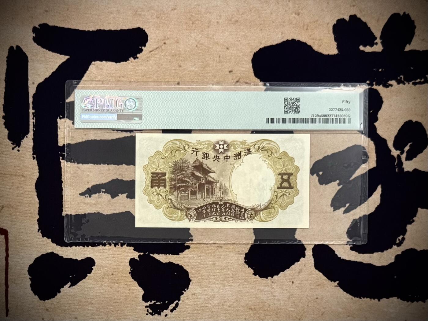 【乾奕收藏】出民国24年1935年满洲中央银行财神爷五角，早期乙号券版本背单线券，相比常见绿财神数量上更少，棕色财神图案，美国PMG50分，民国纸币经过80年能保存如此品相实属难得，喜欢的老板不要错过，评级币一切以分数为准，售出非假不退