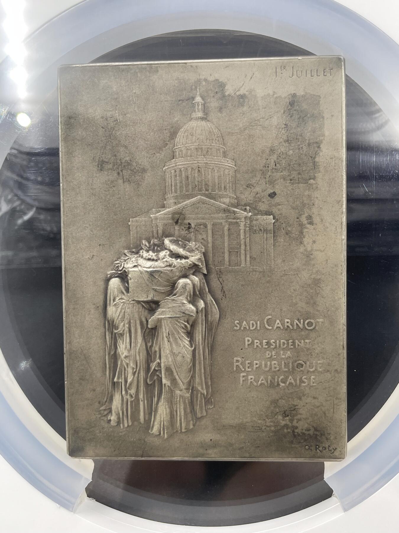 「木头集藏」章牌精品专场！ O Roty～法国卡诺总统葬礼银章，MS62 ，尺寸：81×58mm，155g，边铭：丰饶角 1 ARGENT，NGC评级超大盒，实物品相不错，基本没有明显瑕疵，评分偏低了。马耶尔目录（1870-1940年法国章牌艺术）101号作品。  此章表达了法国全国上下对于深受人民爱戴却不幸遇刺身亡的卡诺总统的哀思。正面图案为玛丽安娜立于花环簇拥的总统遗体旁，背面图案为一群身着长袍黑纱的人将棺椁抬向先贤祠。