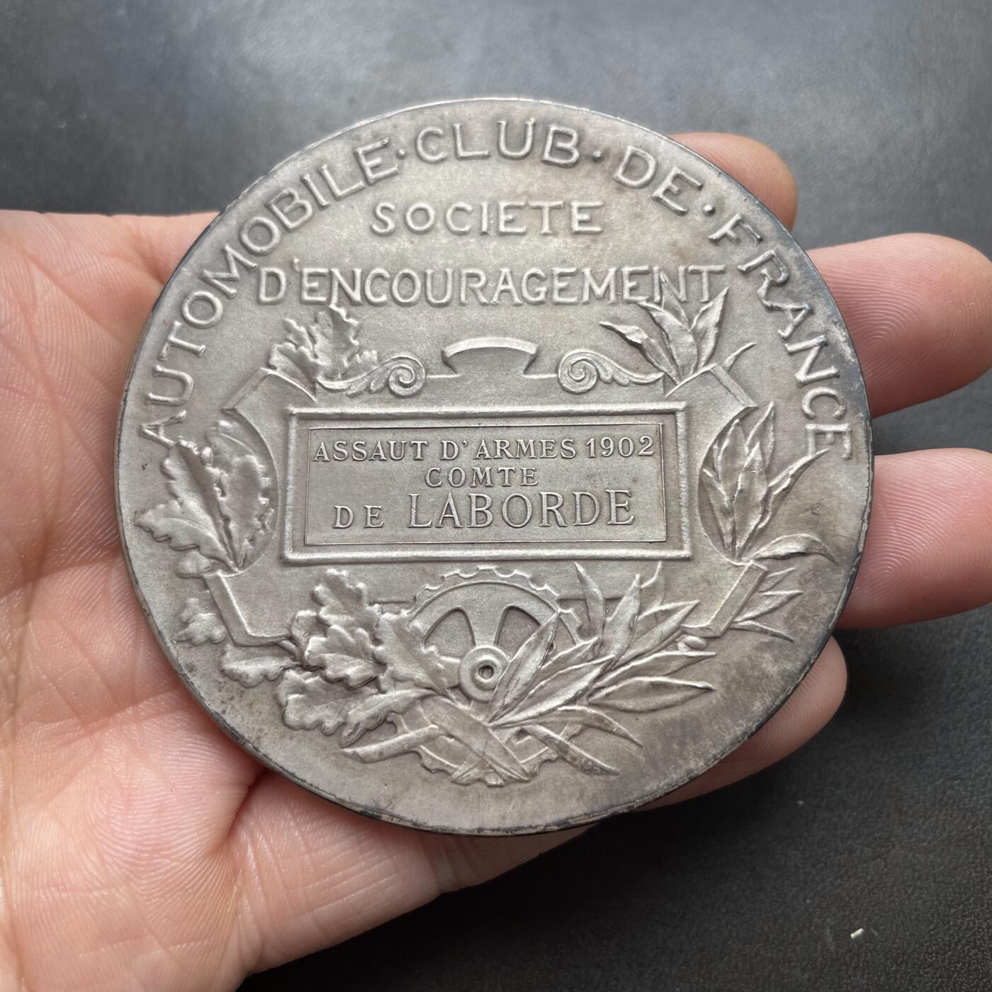 「木头集藏」章牌精品专场！ Daniel Dupuis～1902年法国汽车俱乐部云霄飞车大银章 ，直径：68mm，138g，边铭：丰饶角 ARGENT。经典的清凉美女章，实物品相不错，只是正面包浆不太均匀。根据背面铭文，此章是法国汽车俱乐部在1902年组织的一次剑术精英赛中授予拉博德伯爵的。1902年2月28日的《投石党报》刊文记载了这一盛事：“拉博德伯爵挥舞着剑，赢得了热烈的掌声”。  