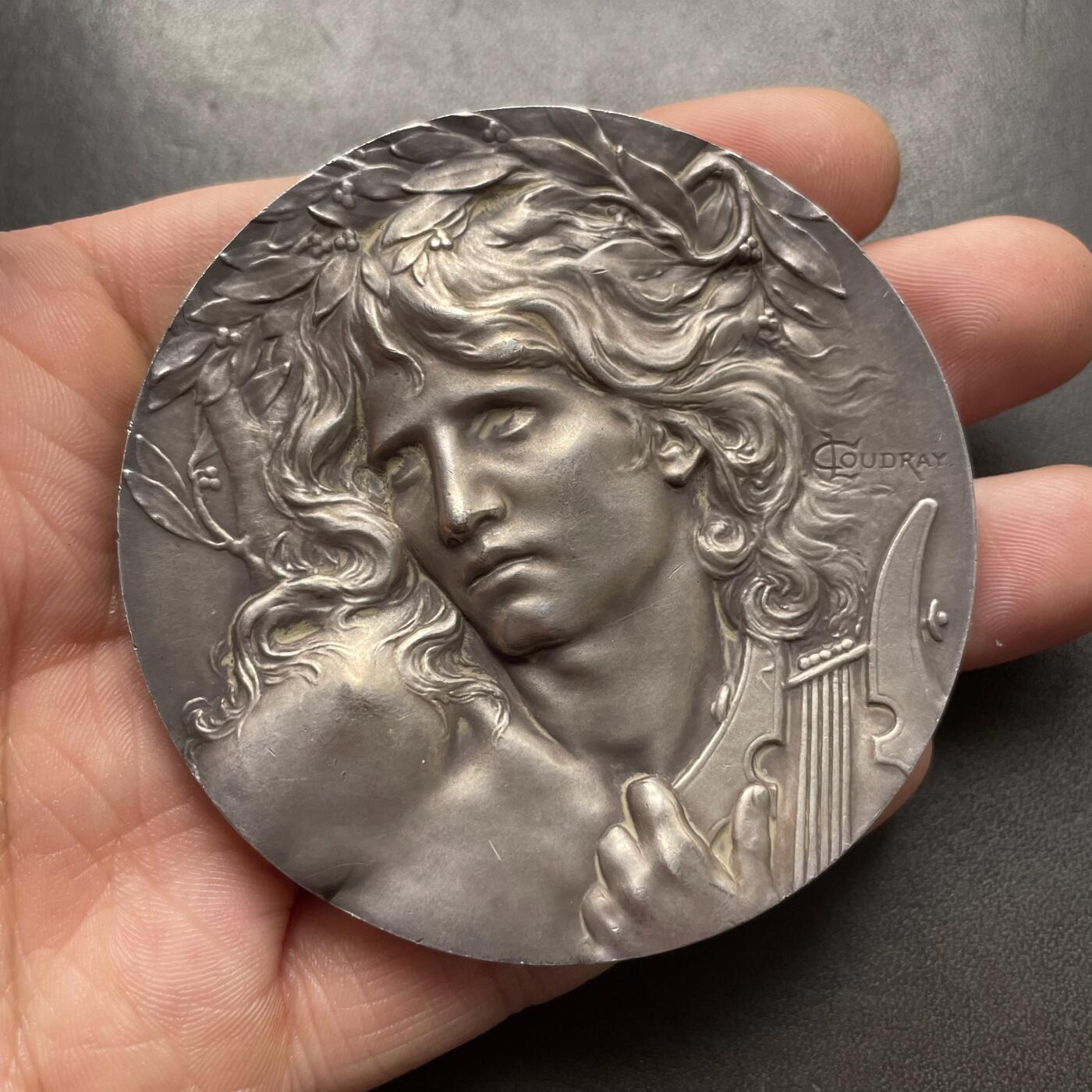 「木头集藏」章牌精品专场！ L.Coudray～法国音乐之神俄尔普斯大银章，直径：68 mm，162.3 g，边铭：丰饶角 ARGENT，名家高浮雕刻画作品，品相不错。俄耳甫斯，是古希腊神话中最著名的音乐家、诗人与先知，以超凡的音乐天赋和悲剧爱情闻名，太阳神阿波罗与缪斯女神卡利俄珀之子