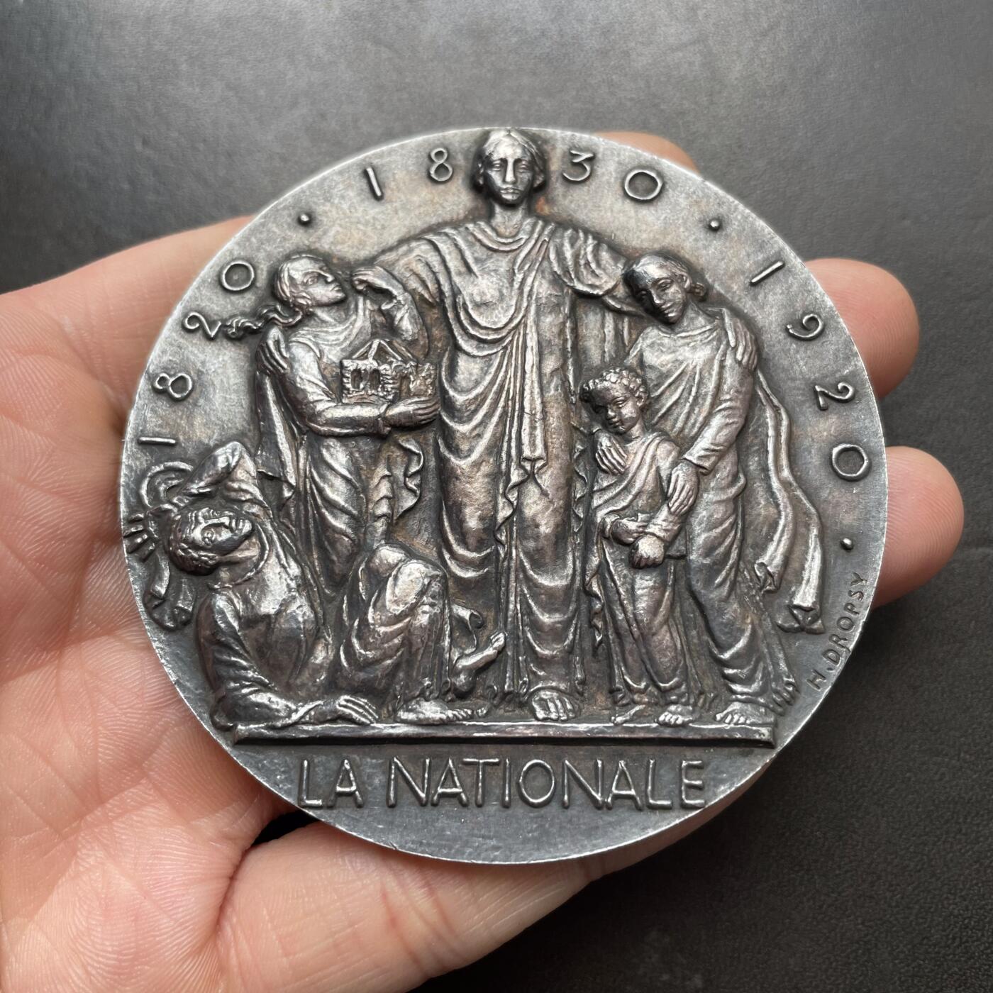 「木头集藏」章牌精品专场！ H. Dropsy～法国国家保险公司大银章 ，直径：70mm，189 g，边铭：菱形厂标+厂名V. CANALE ARGENT 野猪头银标。罕见品种！法国章牌名厂卡纳勒（V Canale）铸造。正面是保险公司化身的女神将老弱妇孺置于自己的庇护之下。法国国家保险公司的前身是1820年成立的皇家人寿保险公司，后重组改为此名。1968年与太阳保险公司和老鹰保险公司合并成为法国国家保险集团。