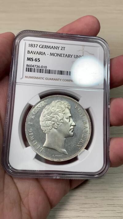 万国钱币拍卖第059期 NGC MS65 1837巴伐利亚路德维希一世货币联盟历史2泰勒 纪念1837年南德六邦在慕尼黑签署《慕尼黑货币协议》，决定停发王冠泰勒，转而以传统的古尔登为单位发行货币，2泰勒面值等于3.5古尔登，而此枚历史2t也就成为了邦国协议2泰勒的开山之作。 类镜面喷砂PL质感顶级BU状态 NGC唯一亚军分
