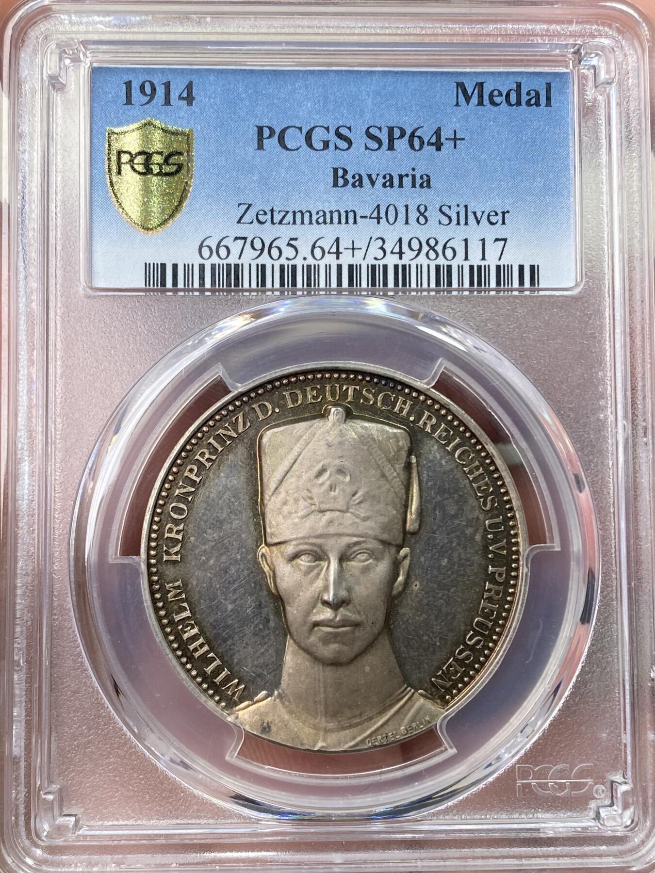 万国钱币拍卖第059期 PCGS SP64+ 1914年德国一战银章 威廉王储/隆维战役 冠军分唯一记录 官网广告封面章 银章评级给+号极为不易，顶级状态。高浮雕，精制底板。紫罗兰浓郁彩虹包浆，绚丽光泽，冰霜图案，微妙的色彩融合极具魅力。正面:威廉王储半身像，身穿骷髅骠骑兵制服。背面:手持帝国鹰徽盾牌和长剑的武士，骑兵在战场上无畏的冲锋。作为威廉皇帝的继承人，他是德意志帝国和普鲁士王国的最后一位王储，直至君主制废除。