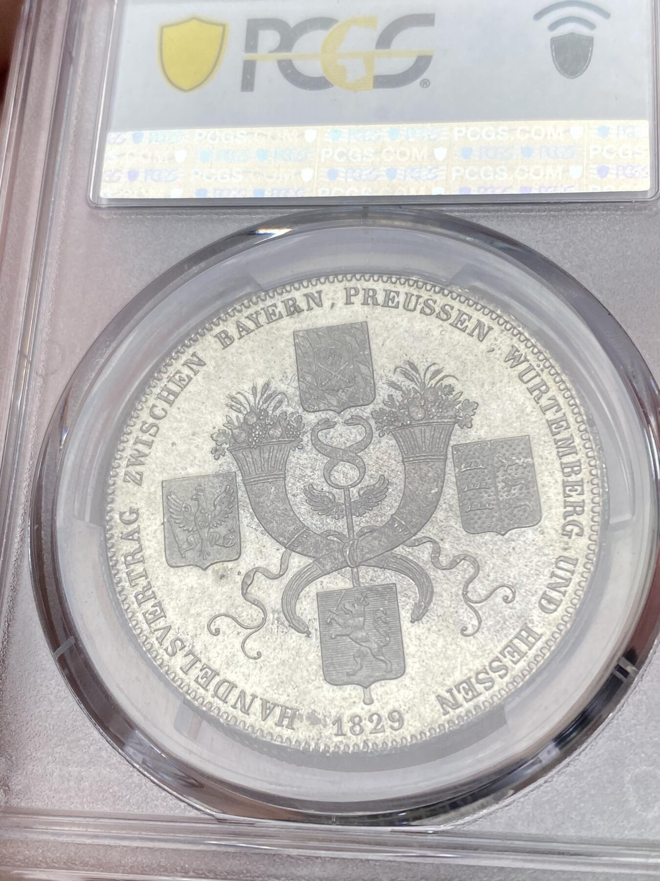 万国钱币拍卖第059期 PCGS MS65 1829年德国巴伐利亚路德维希一世贸易协定历史泰勒  纪念巴伐利亚、普鲁士、符腾堡和黑森之间的贸易协定泰勒 极其难得的BU级别历史大泰勒 银光在币面如流水般泻出  喷砂质感的四邦纹章紧密围绕在象征繁荣富裕的丰饶角周围 实物上手惊艳