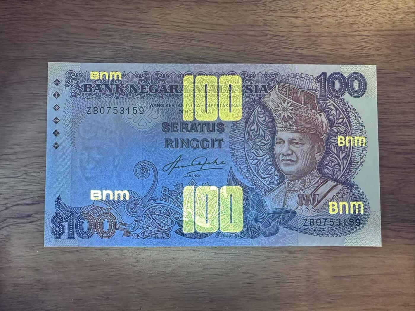 徐霞客拍卖首拍 马来西亚	P-24 1983-84年100元	ZB0753159	unc- 主图为端古·阿卜杜勒·拉赫曼的官方肖像，周围环绕着马来西亚传统花卉纹样与几何装饰，融合了马来文化的精致美学。背面以马来西亚现代化建设成就为主题，通常包含港口、工业区等图案，直观展现了当时经济高速发展的面貌