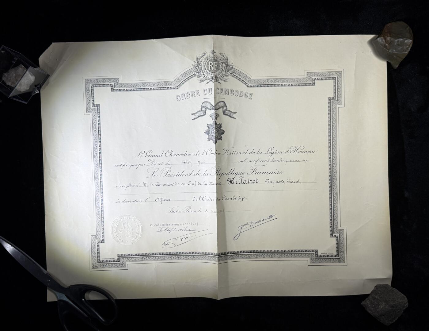 戎马世界章牌大赏第110期 法属柬埔寨王国军官级王冠勋章证书，有折痕破损，属于法国海军专员，有得主相关履历，得主1939年晋升为首席专员，曾在远东的“雷居勒斯号”巡洋舰服役，随后登上“恩特卡斯特奥号”驱逐舰与“巴黎号”战列舰，在“圣女贞德号”巡洋舰度过两年时光后，他曾短暂负责学员晋升考核