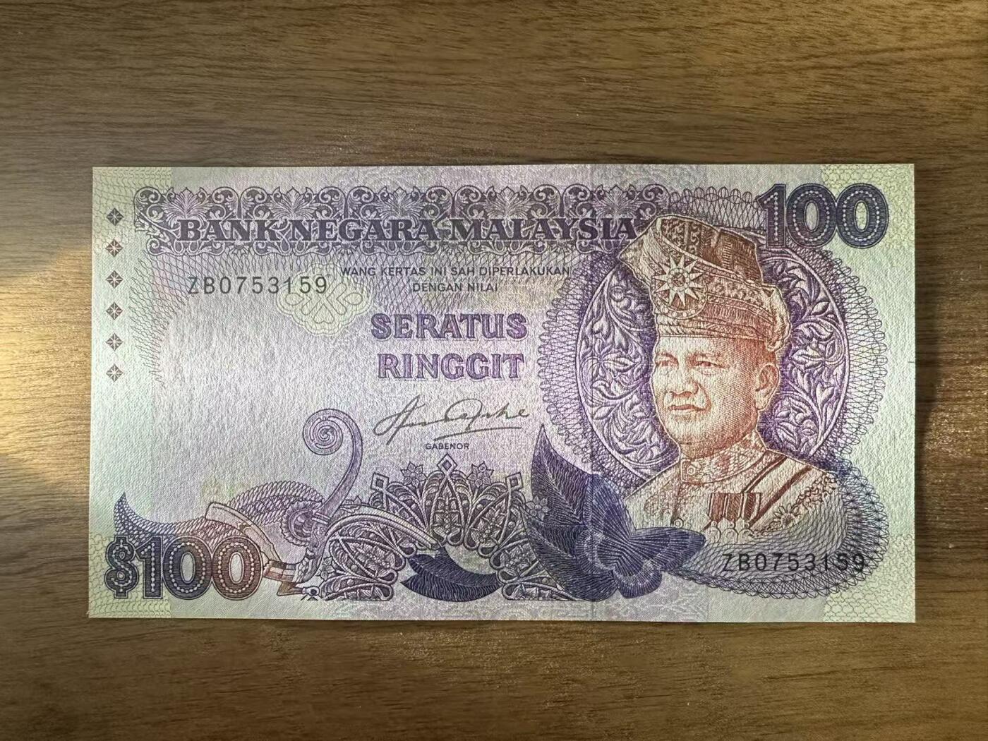 徐霞客拍卖首拍 马来西亚	P-24 1983-84年100元	ZB0753159	unc- 主图为端古·阿卜杜勒·拉赫曼的官方肖像，周围环绕着马来西亚传统花卉纹样与几何装饰，融合了马来文化的精致美学。背面以马来西亚现代化建设成就为主题，通常包含港口、工业区等图案，直观展现了当时经济高速发展的面貌