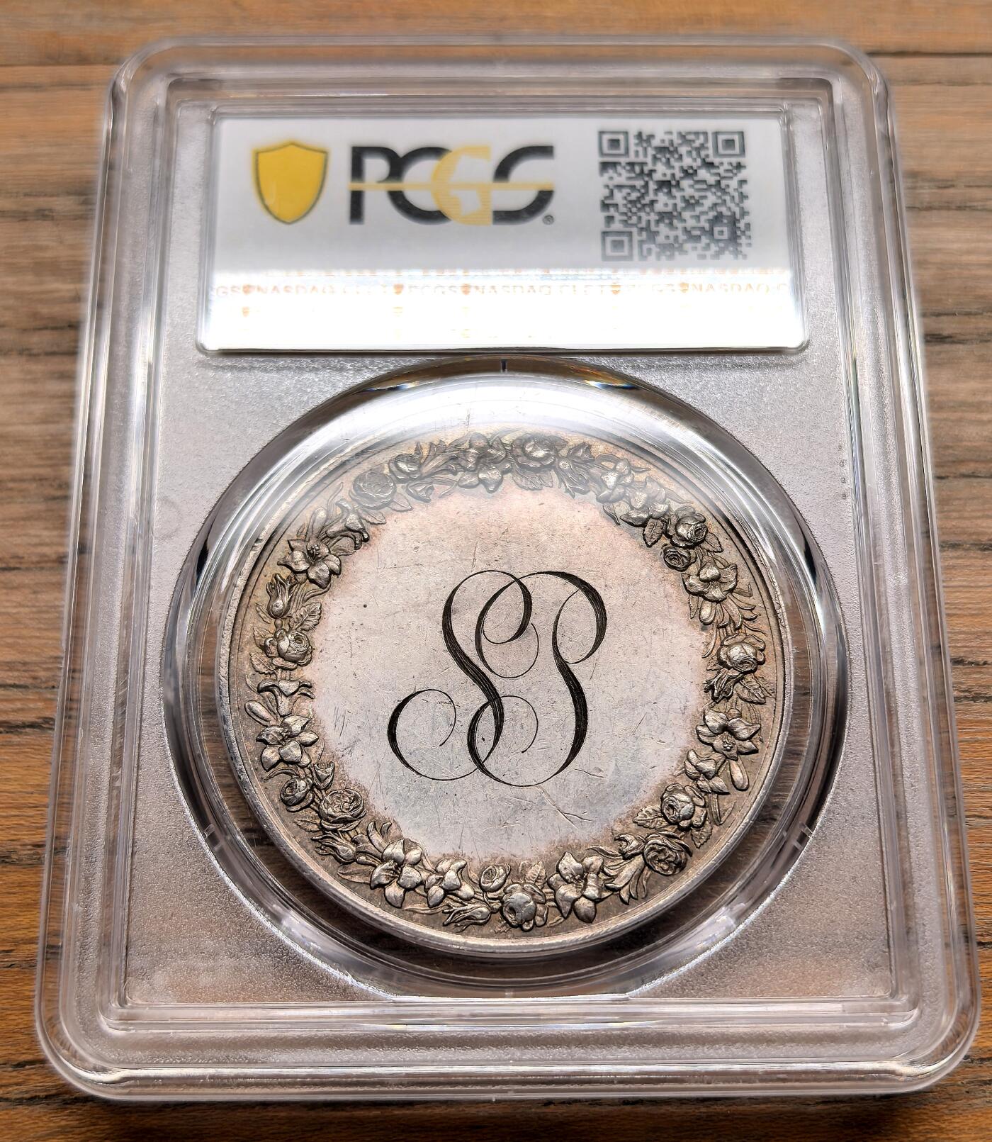 凡希社世界钱币微拍第三百十九期 十九世纪末法国天主教婚姻纪念银章PCGS-MS62，正面是一对古典风格的男女牵手而立，身旁有小狗相伴，背景为砖墙，象征婚姻的陪伴与安稳生活，整体浮雕细腻，充满浪漫主义风格。 背面中央是花押式的字母组合，外围环绕玫瑰花环，象征爱情与婚姻的美好，是当时定制婚礼纪念章的典型布局。