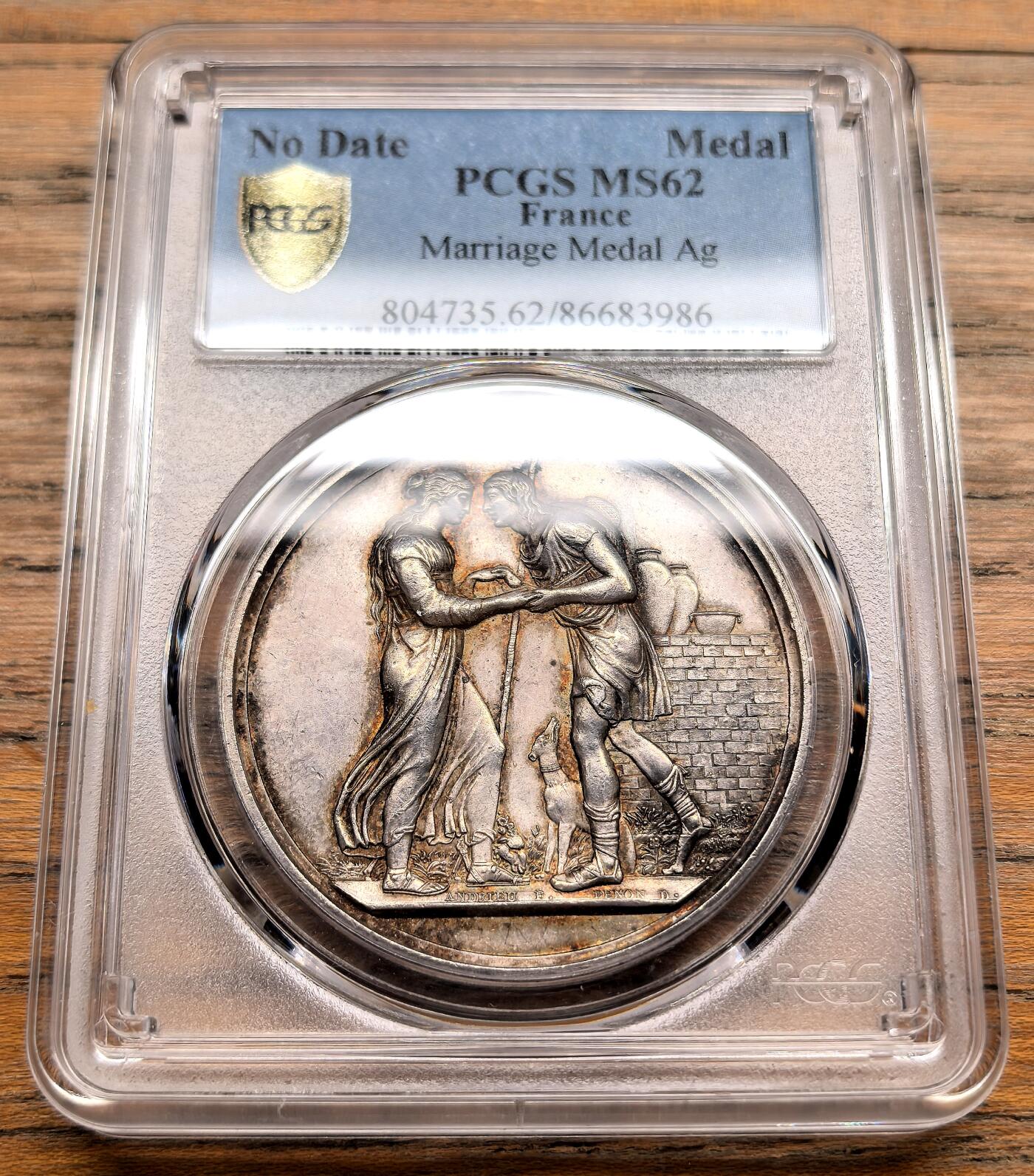 凡希社世界钱币微拍第三百十九期 十九世纪末法国天主教婚姻纪念银章PCGS-MS62，正面是一对古典风格的男女牵手而立，身旁有小狗相伴，背景为砖墙，象征婚姻的陪伴与安稳生活，整体浮雕细腻，充满浪漫主义风格。 背面中央是花押式的字母组合，外围环绕玫瑰花环，象征爱情与婚姻的美好，是当时定制婚礼纪念章的典型布局。