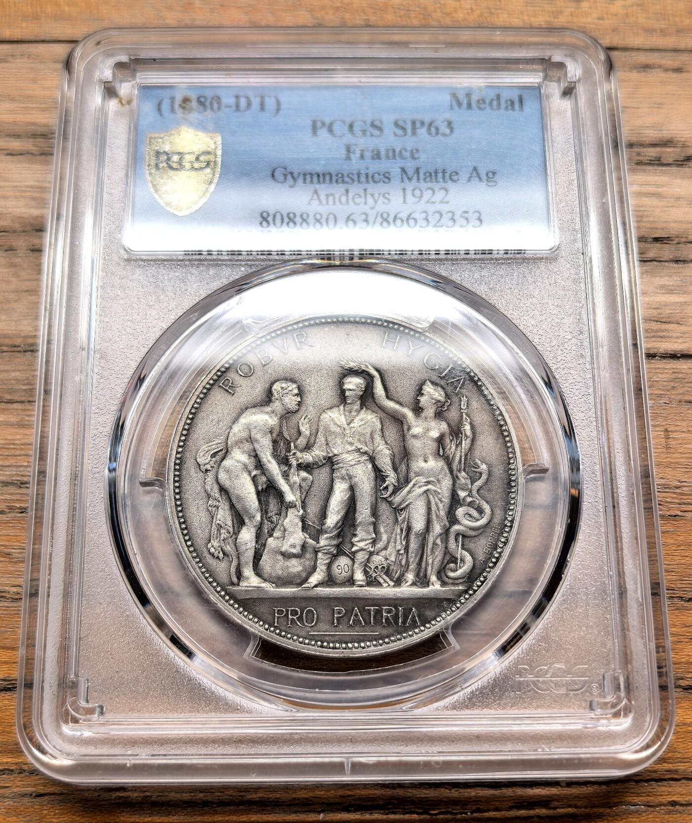 凡希社世界钱币微拍第三百十九期 1922法国昂热利体操运动会哑光工艺银质样章PCGS-SP63，正面浮雕刻画了三位核心人物：左侧是象征力量的男性形象，中间是代表运动员的青年，右侧是手持阿斯克勒庇俄斯之杖（蛇杖）的健康女神许癸厄亚。上方铭文“ROBVR HYGIA”意为“力量与健康”，下方铭文“PRO PATRIA”意为“为了祖国”，体现了当时法国将体育与爱国精神绑定的理念。