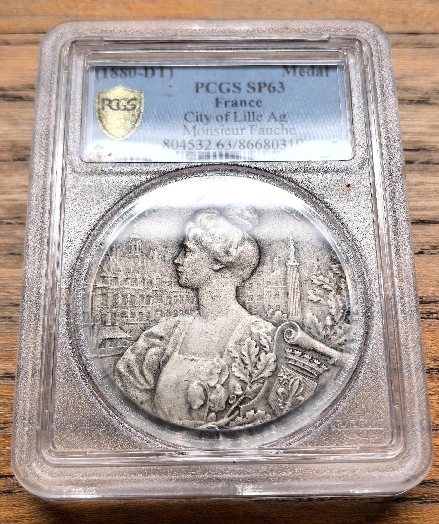 凡希社世界钱币微拍第三百十九期 1880法国里尔市纪念银章PCGS-SP63，-正面浮雕为里尔市的拟人化女性形象，背景是里尔的城市景观，包括标志性的钟楼与古建筑群，边缘装饰有花卉与工业元素，象征里尔的繁荣与活力。