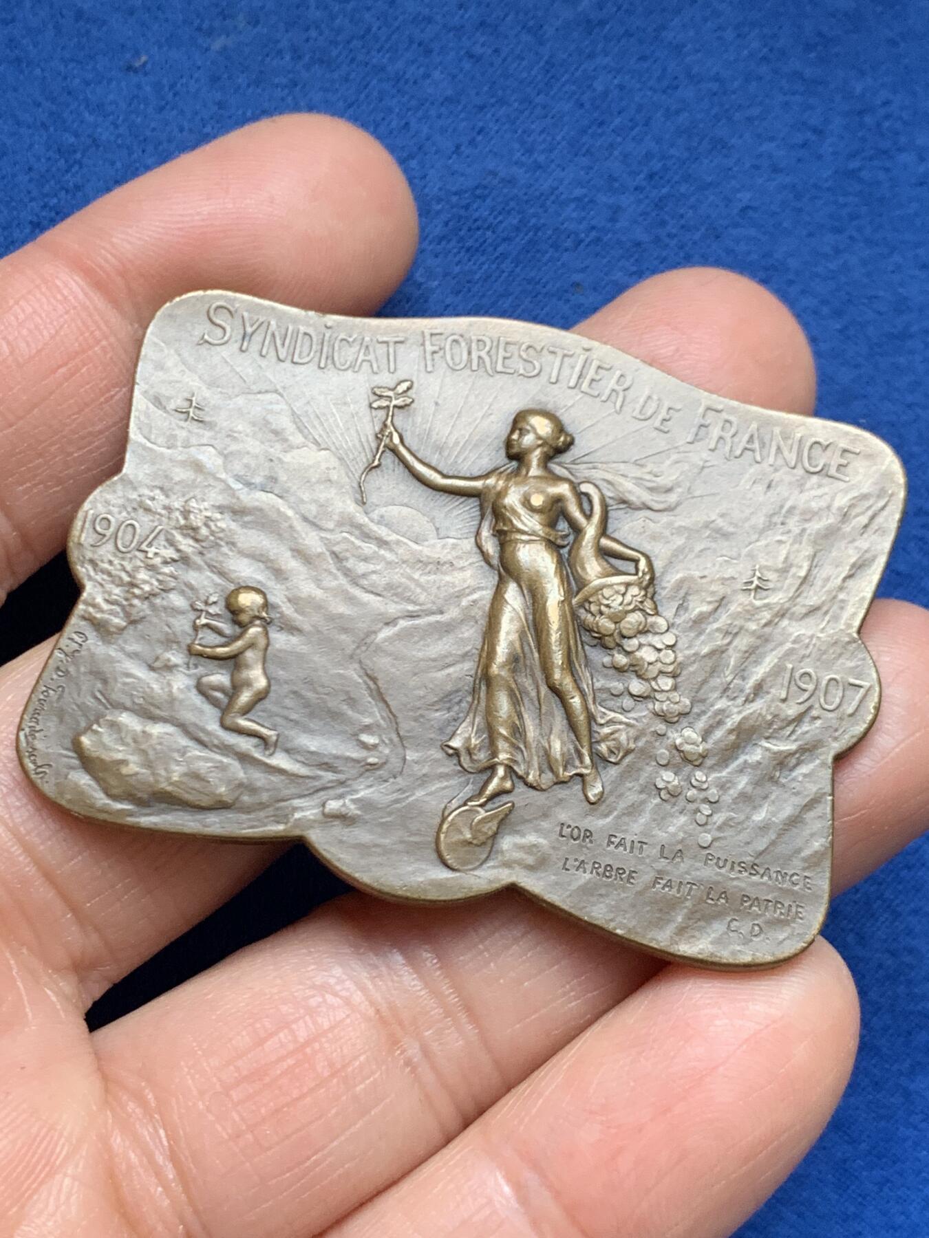 《竞宝斋》第461场 周日，周一，2场连拍 （全场包邮）欢迎送拍 法国1907林业联盟协会铜制异形奖章，首见款。正面：春之女神右手挽鲜花，左手播种树苗，脚踏风火轮，底部一个小天使在种植树苗。直径：53.6mm*40.8mm，重：38.2g，丰饶角铜标。