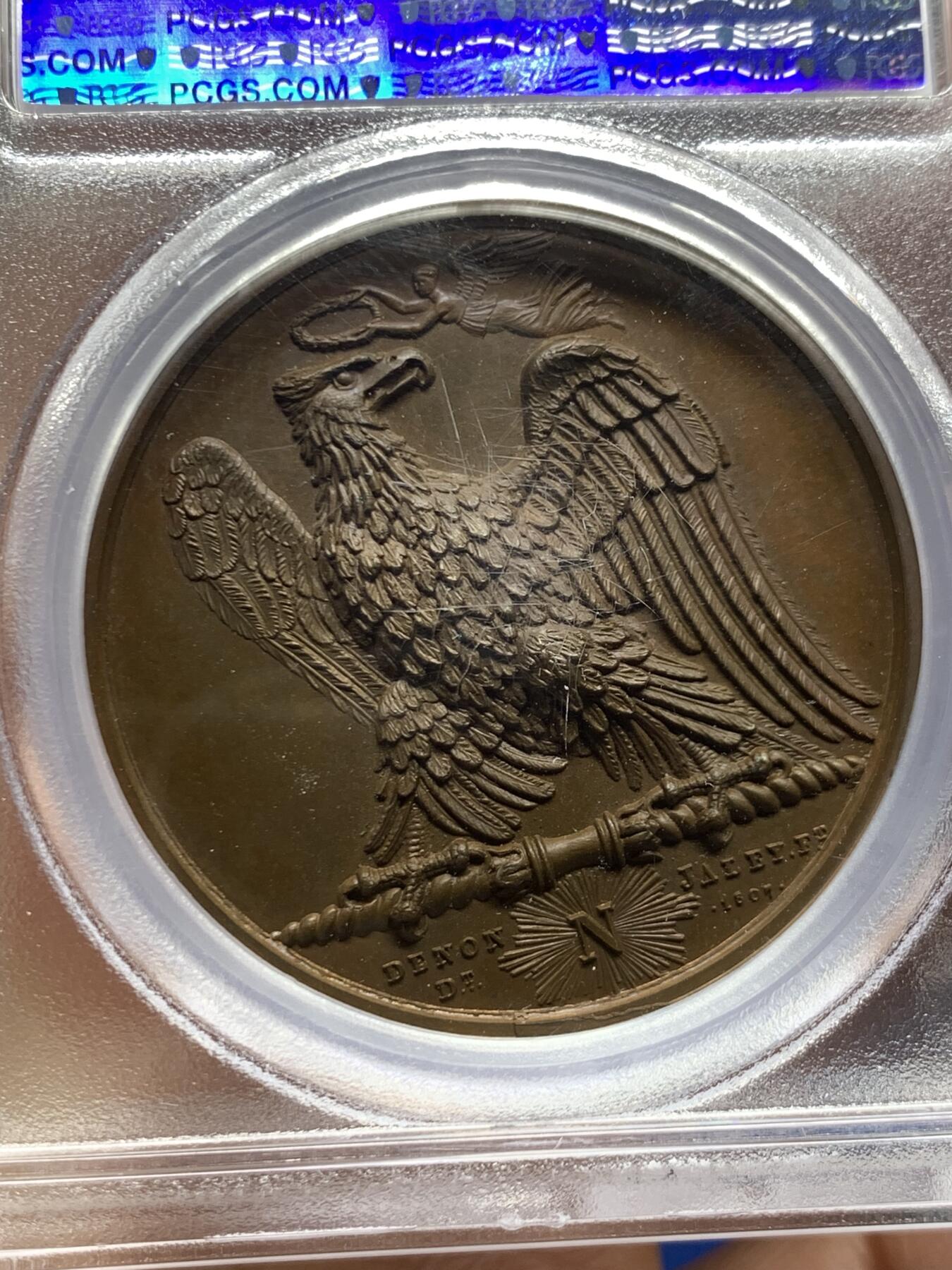 《竞宝斋》第461场 周日，周一，2场连拍 （全场包邮）欢迎送拍 PCGS SP65 冠军分！法国1807年拿破仑一世年度胜利原铸铜章 巴黎造币厂 巧克力包浆 帝国之鹰展翅爪子锋利 紧紧攥住矗立于N记雷电权杖之上 目光锐利如炬 羽翼丰满 丝缕清晰细节感人 作为拿皇的拟人化象征 接受上空胜利女神飞舞空中送来月桂花环为其加冕 作为年度总结庆祝过去的一年中军队获取的胜利 稀少珍贵品种 加厚盒