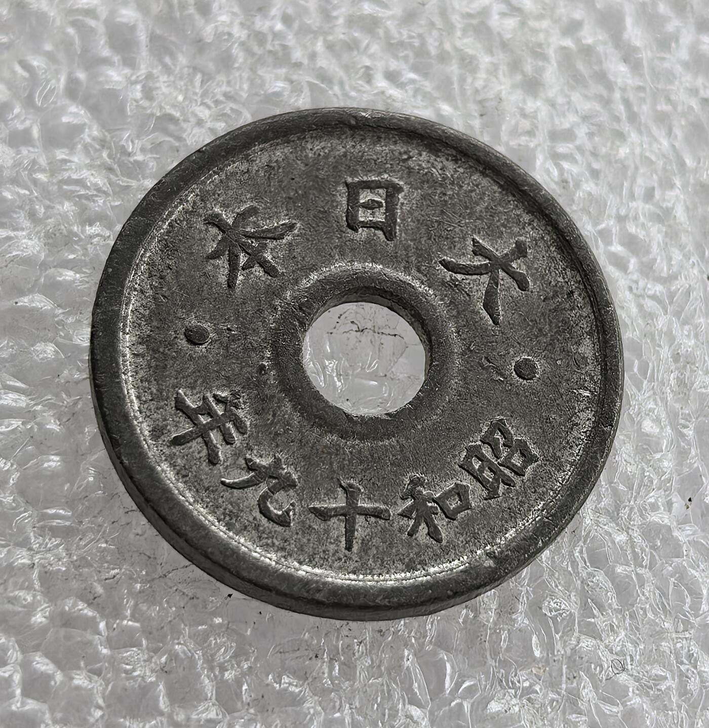 外国优质老铜币高银银币，周六九点倒数截拍，满百包邮，持续收拍 极美品昭和十九年（1944 年）日本五钱锡币，正面皇室菊纹彰显皇权，桐叶祥云纹为传统装饰，圆孔形制节省材料；背面 “大日本”“昭和十九年” 标注国名与年号。二战末期日本金属资源匮乏，改用锡铸币，是战时经济崩溃、军国主义走向末路的货币见证