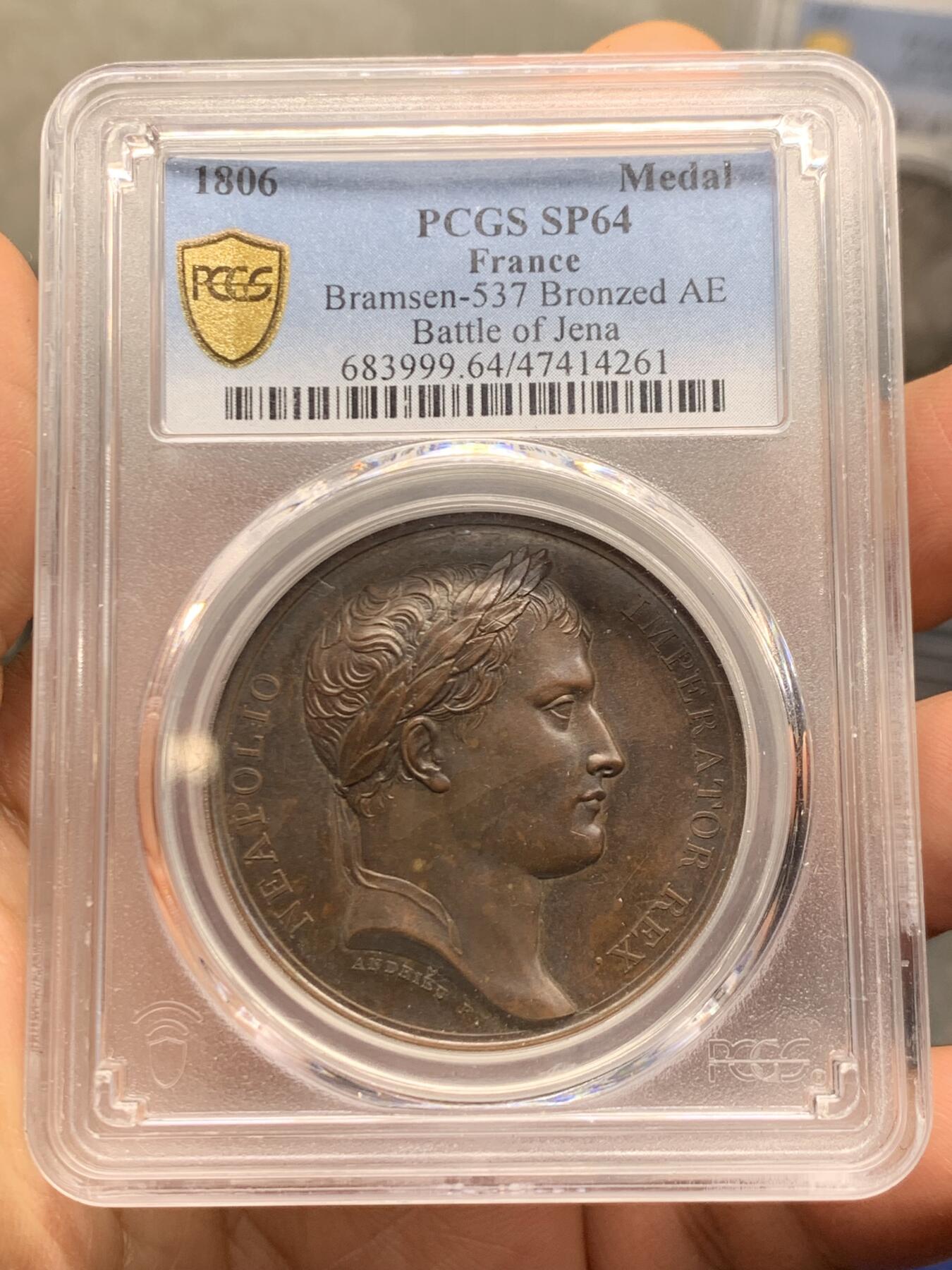 《竞宝斋》第462场 周日，周一，2场连拍 （全场包邮）欢迎送拍 PCGS SP64 亚军分！ 法国1806年拿破仑一世耶拿之战原铸铜章 巴黎造币厂极美巧克力包浆 拿破仑头戴月桂冠 身穿古罗马凯撒式战袍 骑着高头大马 手持雷电 冲锋追击普鲁士溃逃之敌 其一已倒地命丧黄泉 剩下一人作跪地求饶状 帝国之鹰在头顶呼应盘旋向前 1806年耶拿之战拿破仑指挥法军在耶拿和魏玛地区大败普鲁士 画面雕刻细腻生动 拿皇英明神武之气概溢于言表 仅一枚65分更高 加厚盒