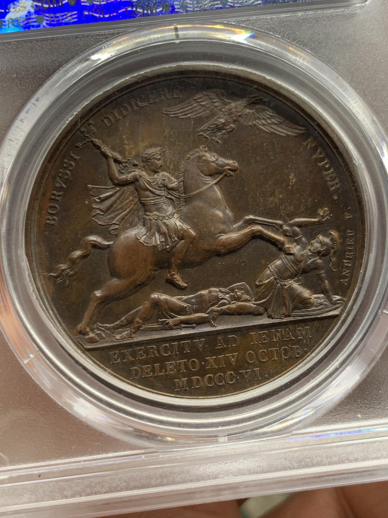 《竞宝斋》第462场 周日，周一，2场连拍 （全场包邮）欢迎送拍 PCGS SP64 亚军分！ 法国1806年拿破仑一世耶拿之战原铸铜章 巴黎造币厂极美巧克力包浆 拿破仑头戴月桂冠 身穿古罗马凯撒式战袍 骑着高头大马 手持雷电 冲锋追击普鲁士溃逃之敌 其一已倒地命丧黄泉 剩下一人作跪地求饶状 帝国之鹰在头顶呼应盘旋向前 1806年耶拿之战拿破仑指挥法军在耶拿和魏玛地区大败普鲁士 画面雕刻细腻生动 拿皇英明神武之气概溢于言表 仅一枚65分更高 加厚盒