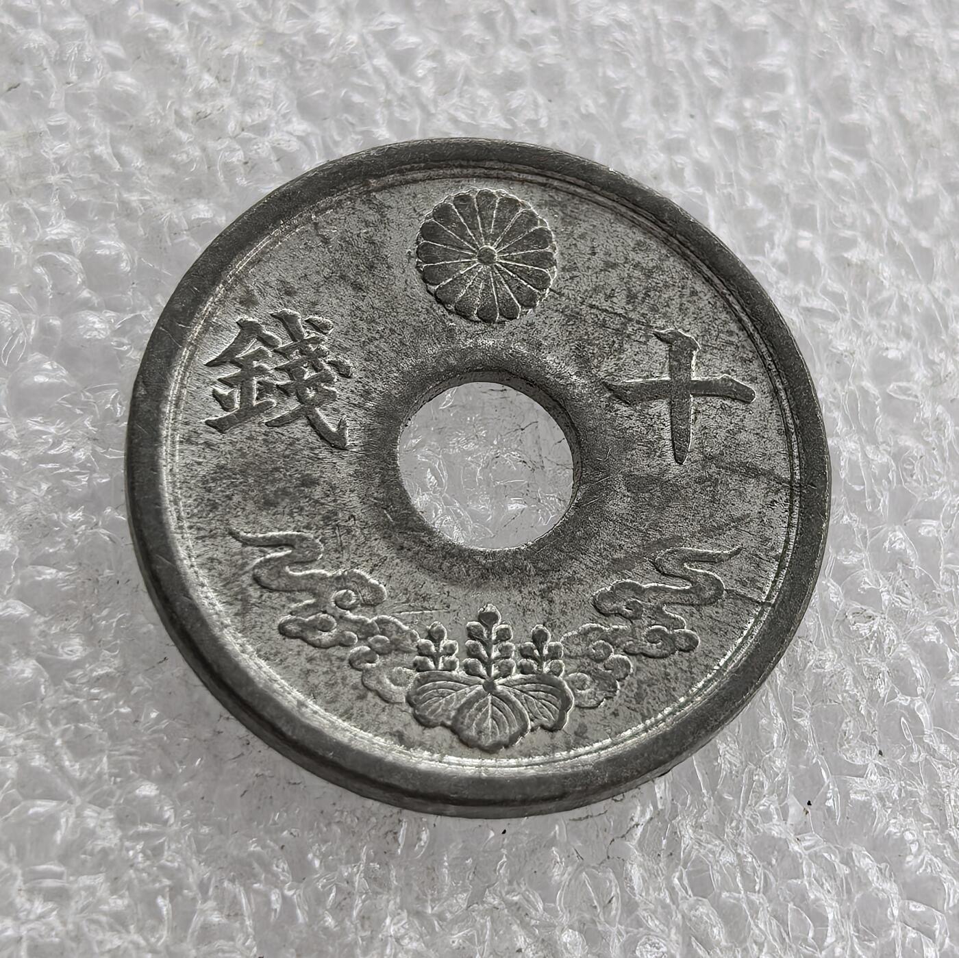 外国优质老铜币高银银币，周六九点倒数截拍，满百包邮，持续收拍 极美品昭和十九年（1944 年）日本十钱锡币，正面皇室菊纹、桐叶祥云纹彰显皇权与传统，圆孔形制节省材料；背面 “大日本”“昭和十九年” 标注国名年号，是二战末期日本金属匮乏、战时经济崩溃的货币见证。