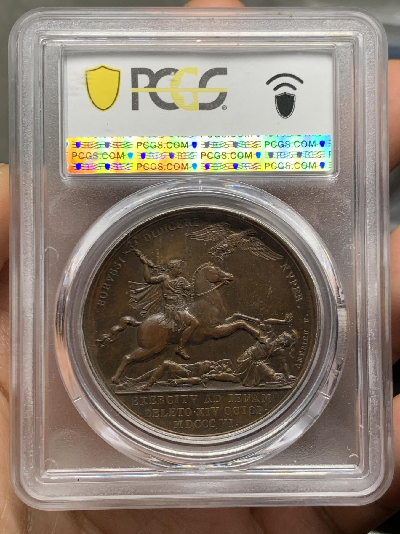 《竞宝斋》第462场 周日，周一，2场连拍 （全场包邮）欢迎送拍 PCGS SP64 亚军分！ 法国1806年拿破仑一世耶拿之战原铸铜章 巴黎造币厂极美巧克力包浆 拿破仑头戴月桂冠 身穿古罗马凯撒式战袍 骑着高头大马 手持雷电 冲锋追击普鲁士溃逃之敌 其一已倒地命丧黄泉 剩下一人作跪地求饶状 帝国之鹰在头顶呼应盘旋向前 1806年耶拿之战拿破仑指挥法军在耶拿和魏玛地区大败普鲁士 画面雕刻细腻生动 拿皇英明神武之气概溢于言表 仅一枚65分更高 加厚盒