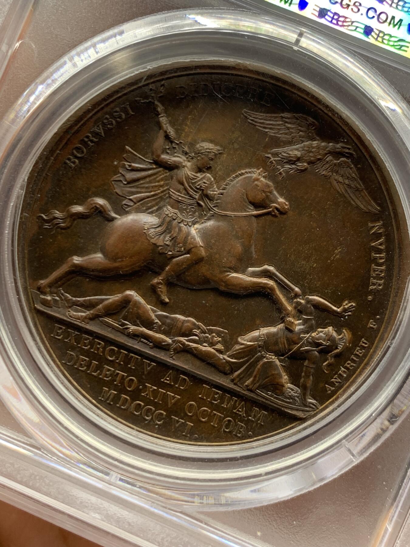 《竞宝斋》第462场 周日，周一，2场连拍 （全场包邮）欢迎送拍 PCGS SP64 亚军分！ 法国1806年拿破仑一世耶拿之战原铸铜章 巴黎造币厂极美巧克力包浆 拿破仑头戴月桂冠 身穿古罗马凯撒式战袍 骑着高头大马 手持雷电 冲锋追击普鲁士溃逃之敌 其一已倒地命丧黄泉 剩下一人作跪地求饶状 帝国之鹰在头顶呼应盘旋向前 1806年耶拿之战拿破仑指挥法军在耶拿和魏玛地区大败普鲁士 画面雕刻细腻生动 拿皇英明神武之气概溢于言表 仅一枚65分更高 加厚盒