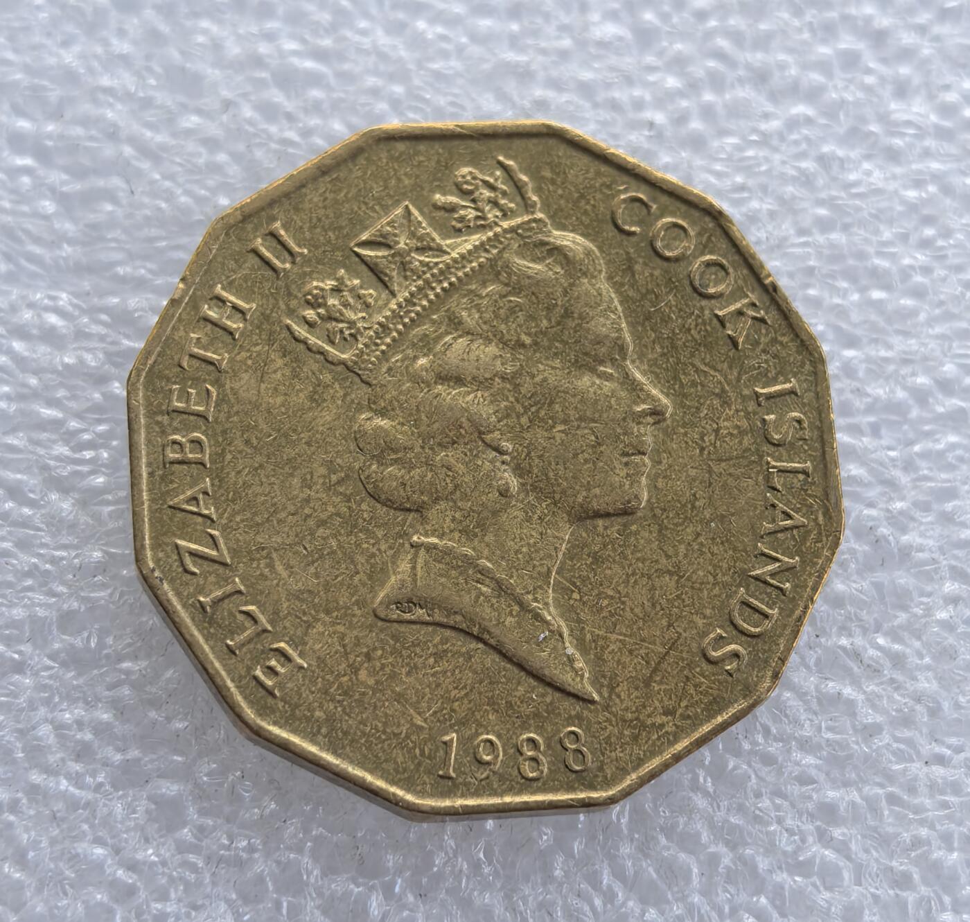 外国优质老铜币高银银币，周六九点倒数截拍，满百包邮，持续收拍 库克群岛1988 年5 元黄铜纪念 / 流通币，采用十二边形独特形制。正面为伊丽莎白二世头像，标注 “COOK ISLANDS” 与年份；背面铸海螺图案及面值 $5，海螺是南太平洋地域象征，属英联邦海外领地特色钱币。