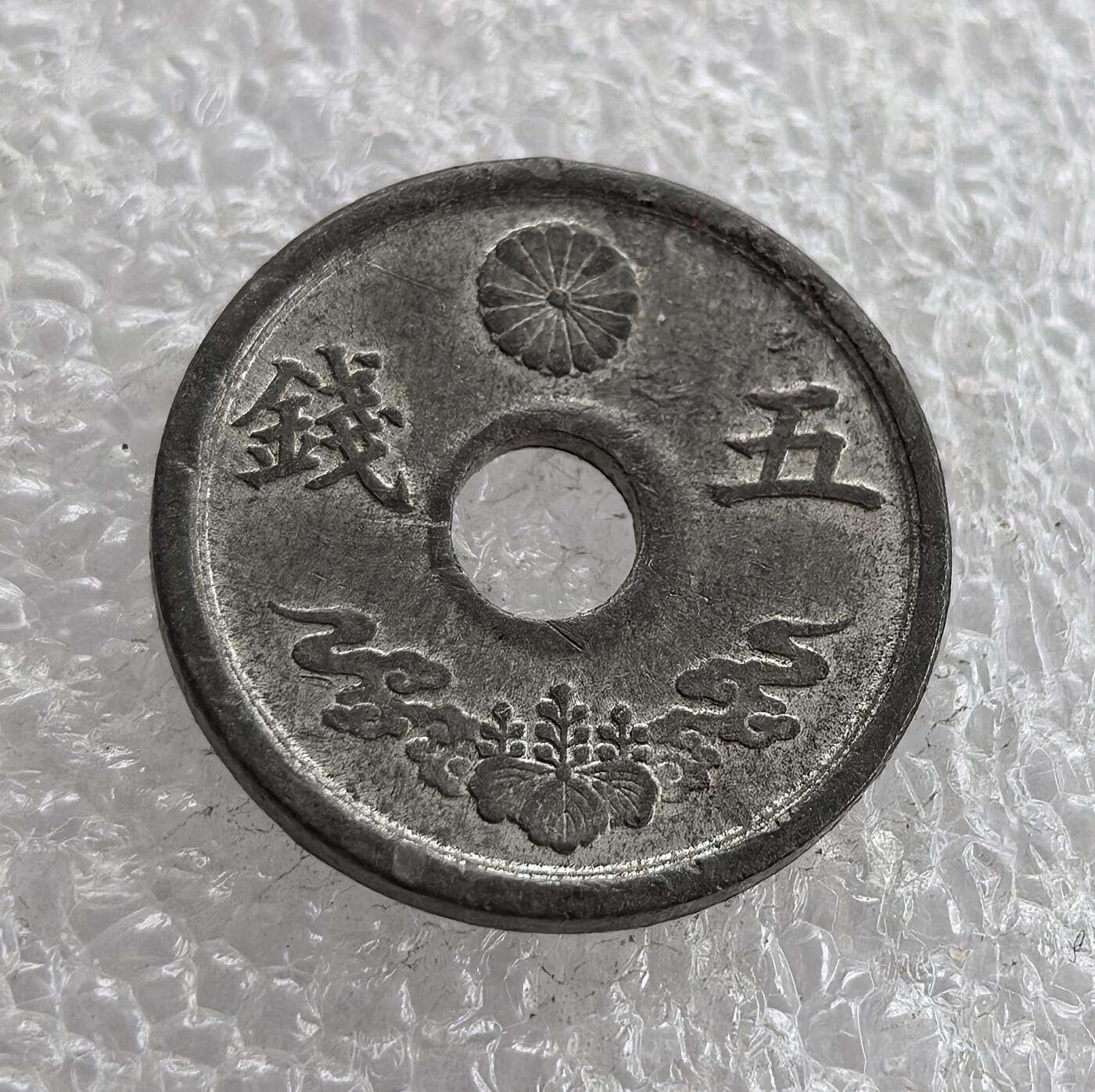 外国优质老铜币高银银币，周六九点倒数截拍，满百包邮，持续收拍 极美品昭和十九年（1944 年）日本五钱锡币，正面皇室菊纹彰显皇权，桐叶祥云纹为传统装饰，圆孔形制节省材料；背面 “大日本”“昭和十九年” 标注国名与年号。二战末期日本金属资源匮乏，改用锡铸币，是战时经济崩溃、军国主义走向末路的货币见证