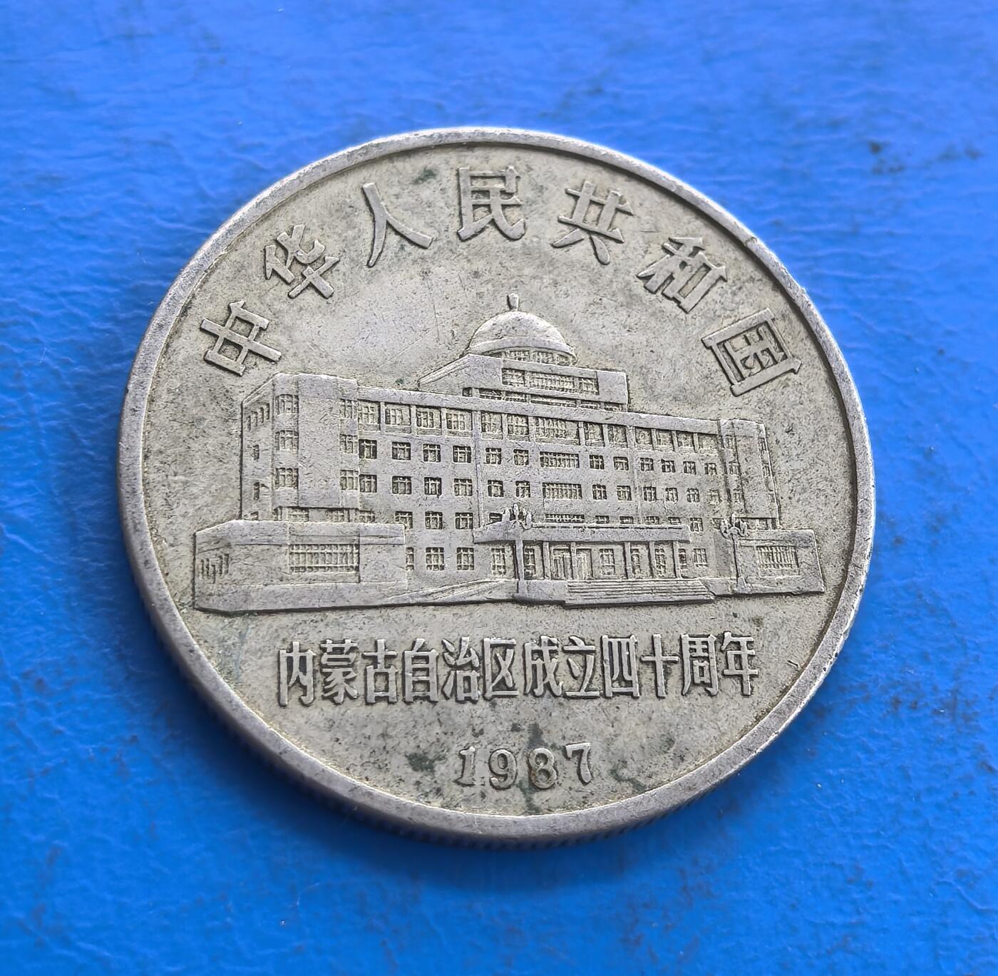 外国优质老铜币高银银币，周六九点倒数截拍，满百包邮，持续收拍 内蒙古自治区1987 年成立四十周年 1 元纪念币，正面铸政府大楼与纪念文字，背面刻画牧民骑马、羊群场景，蒙文与年份点缀，雕刻细腻，民族风情浓郁，兼具历史纪念价值与工艺美感。