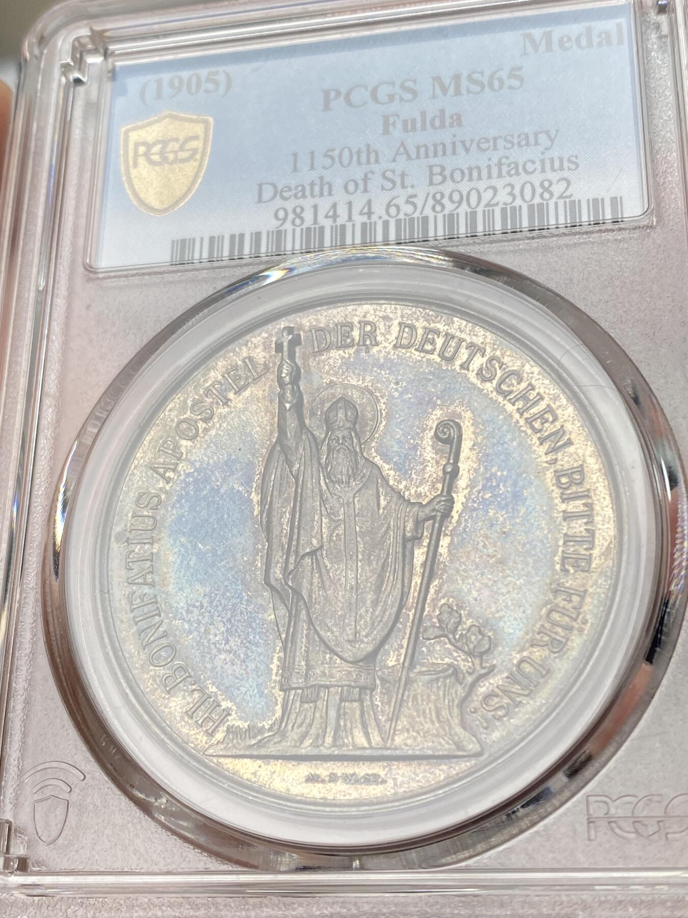 万国钱币拍卖第060期（万国六十期纪念大拍） PCGS MS65 1905年德国黑森富尔达圣博尼法斯逝世1150年纪念银章 稀有品种 唯一评级记录冠军分 浮雕精铸，百年纸袋彩浆。正面:圣博尼法斯全身像，右手举着十字架，左手拿着传道权杖，日耳曼尼亚的守护神。朱庇特万神之王圣橡树被砍倒后发出了新芽。背面:三叶草圈环内的三面盾徽。朱庇特万神之王橡树是日耳曼教徒的一棵圣树。圣树受到日耳曼各民族的广泛崇敬，其木材被用来在圣彼得教堂的原址建造教堂。